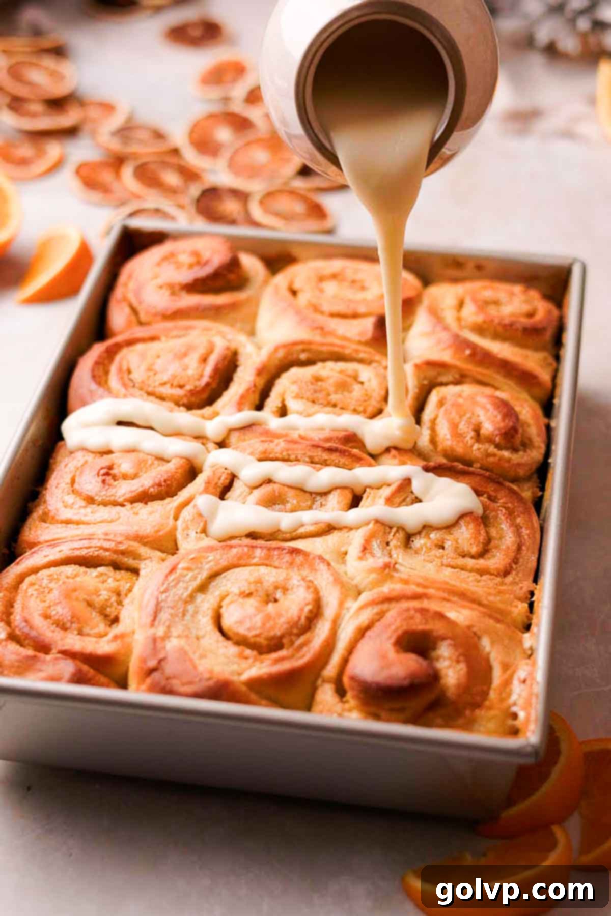 pouring glaze over orange cinnamon rolls