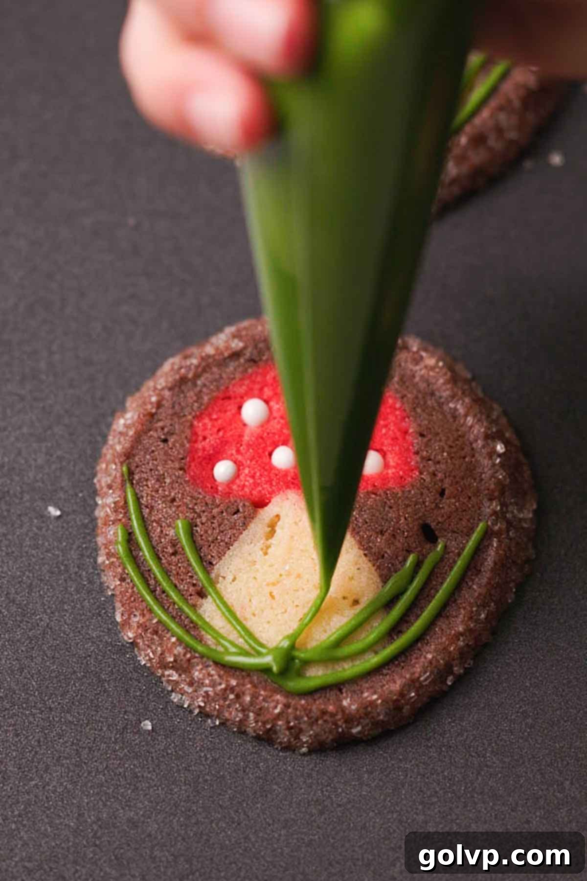 piping green grass frosting onto the base of a mushroom cookie