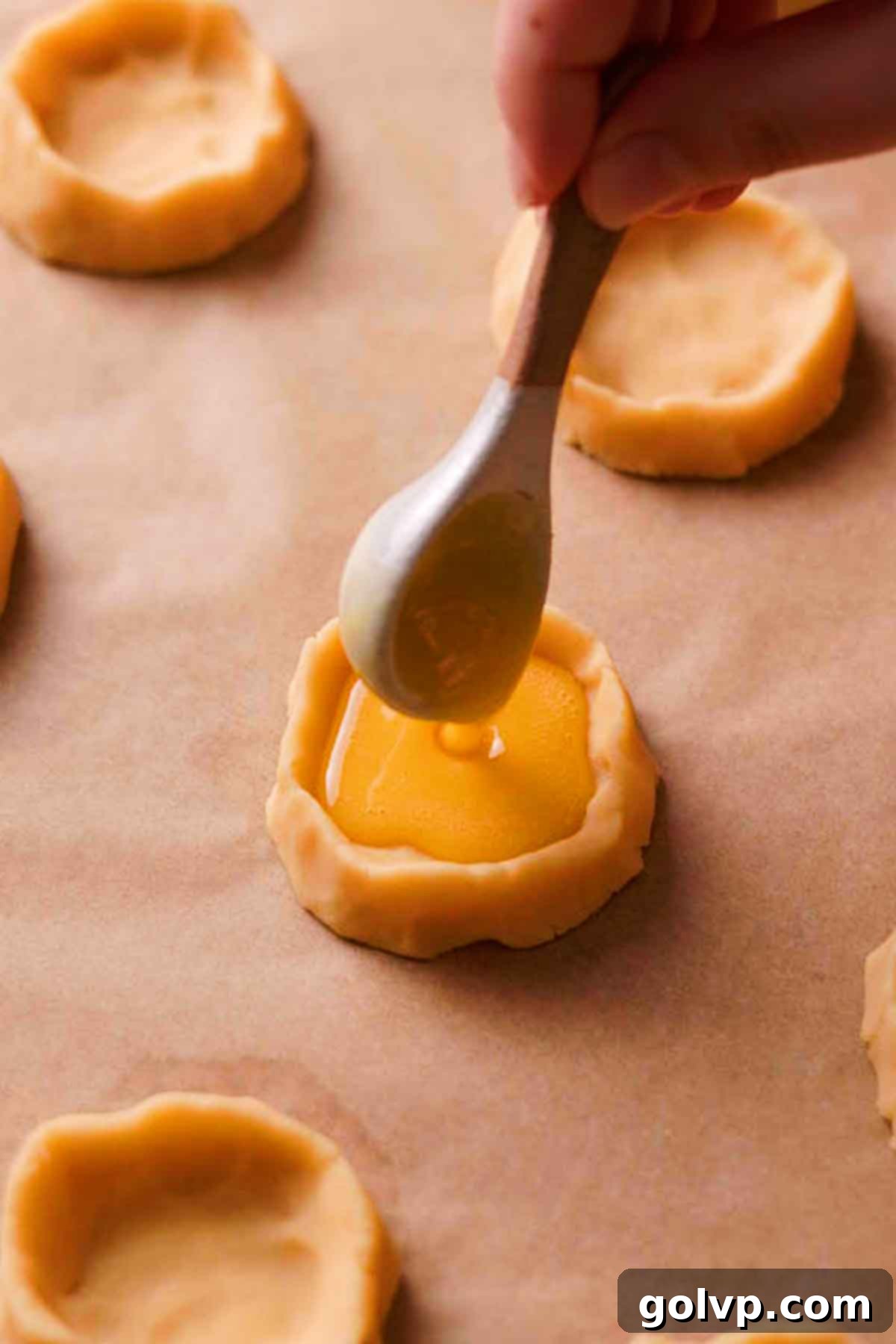 Using a spoon to carefully fill the shortbread cookie cups with the prepared lemon filling on a baking sheet