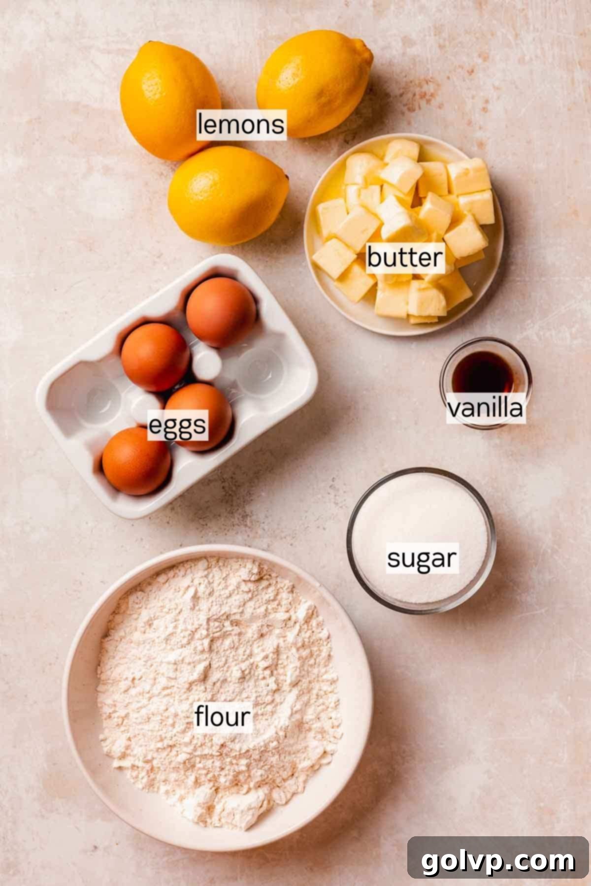 A flat lay of all the fresh ingredients needed for lemon meringue pie cookies including lemons, eggs, butter, sugar, and flour