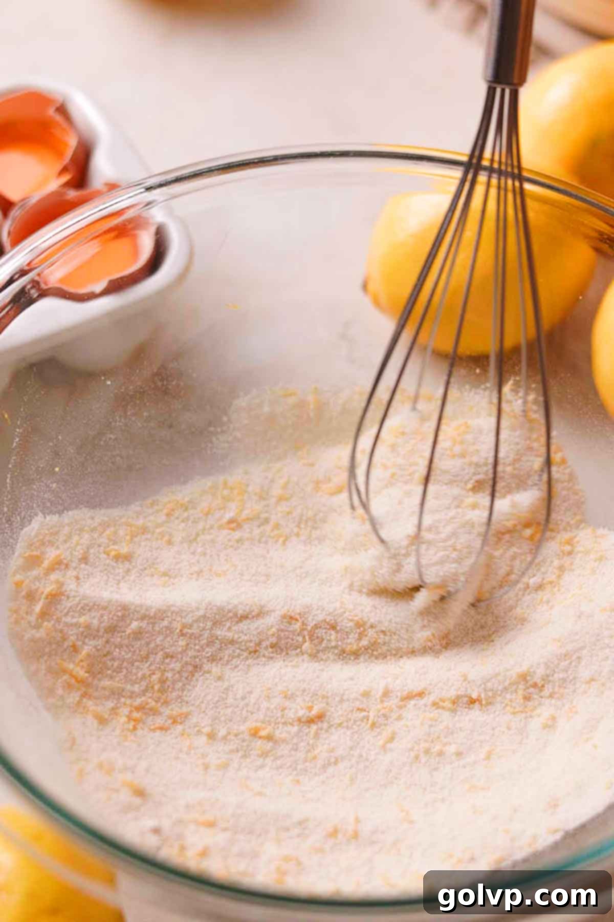 Whisking together granulated sugar, flour, and lemon zest in a glass bowl for the lemon cookie filling