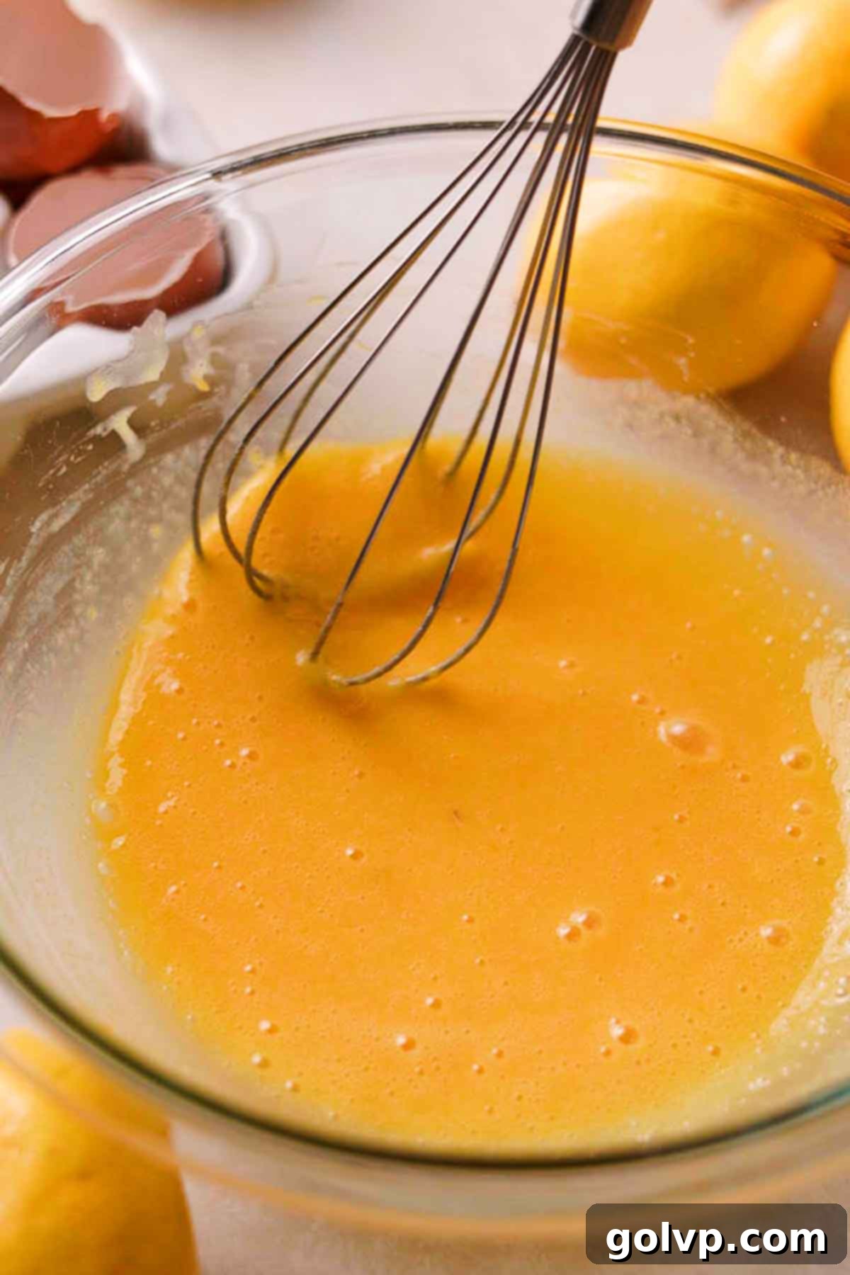 Whisking egg yolks and fresh lemon juice into the dry ingredients for the lemon bar filling in a glass bowl