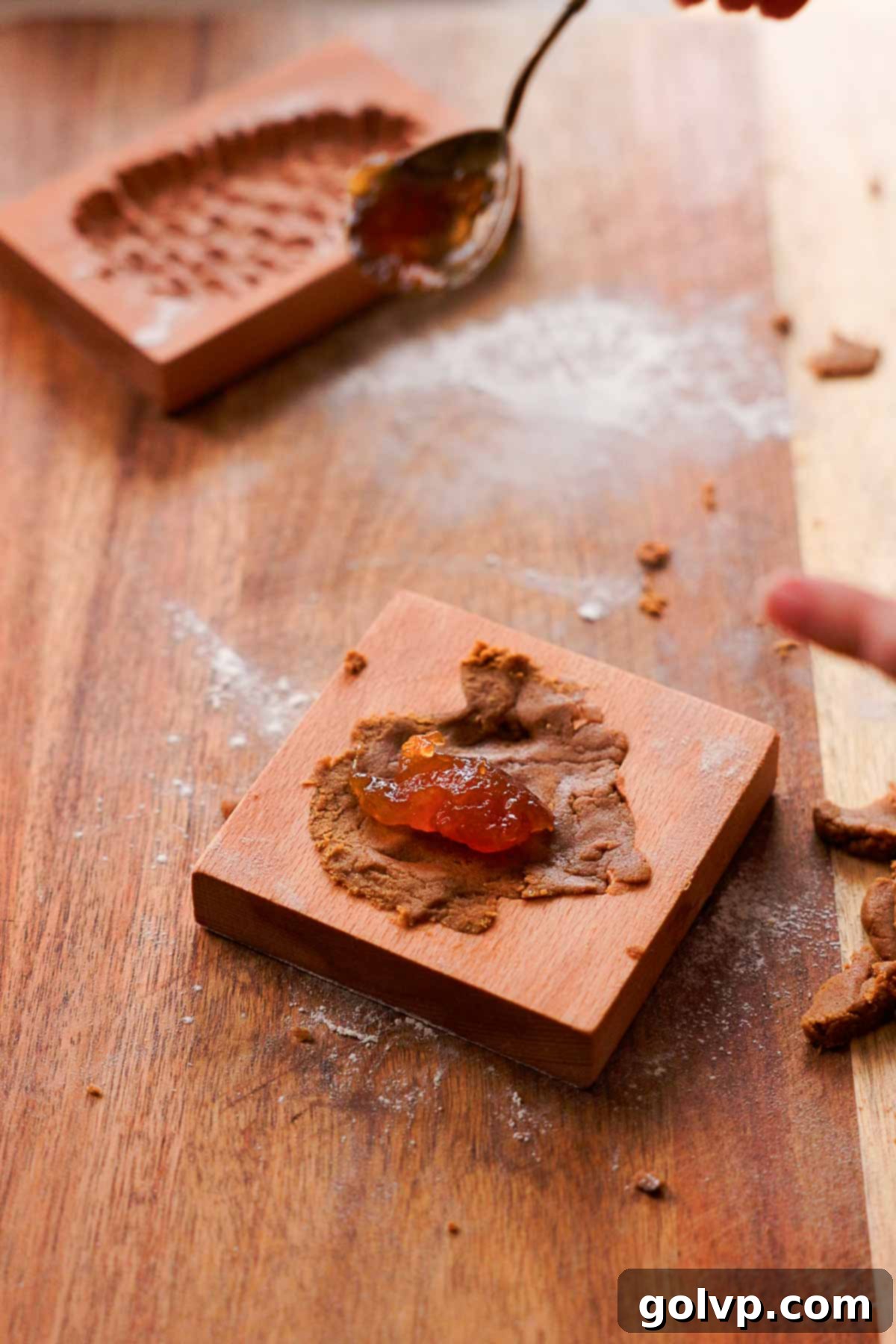 adding a teaspoonful of jam into the center of gingerbread cookie dough inside a wooden cookie mold