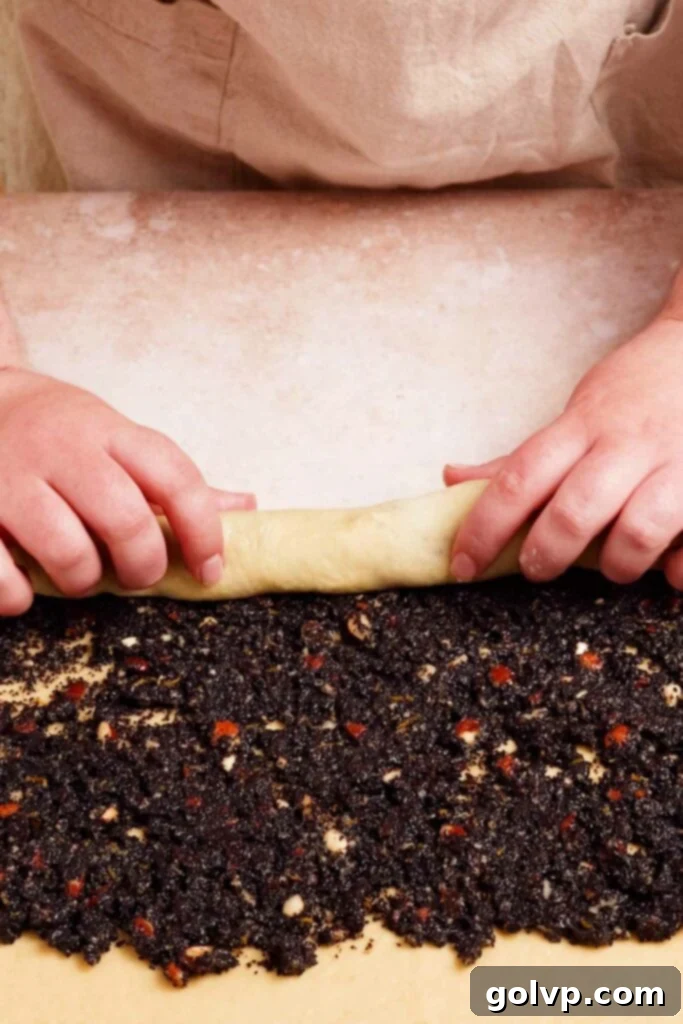 Hands carefully rolling a poppy seed filled dough into a log on a lightly floured surface.