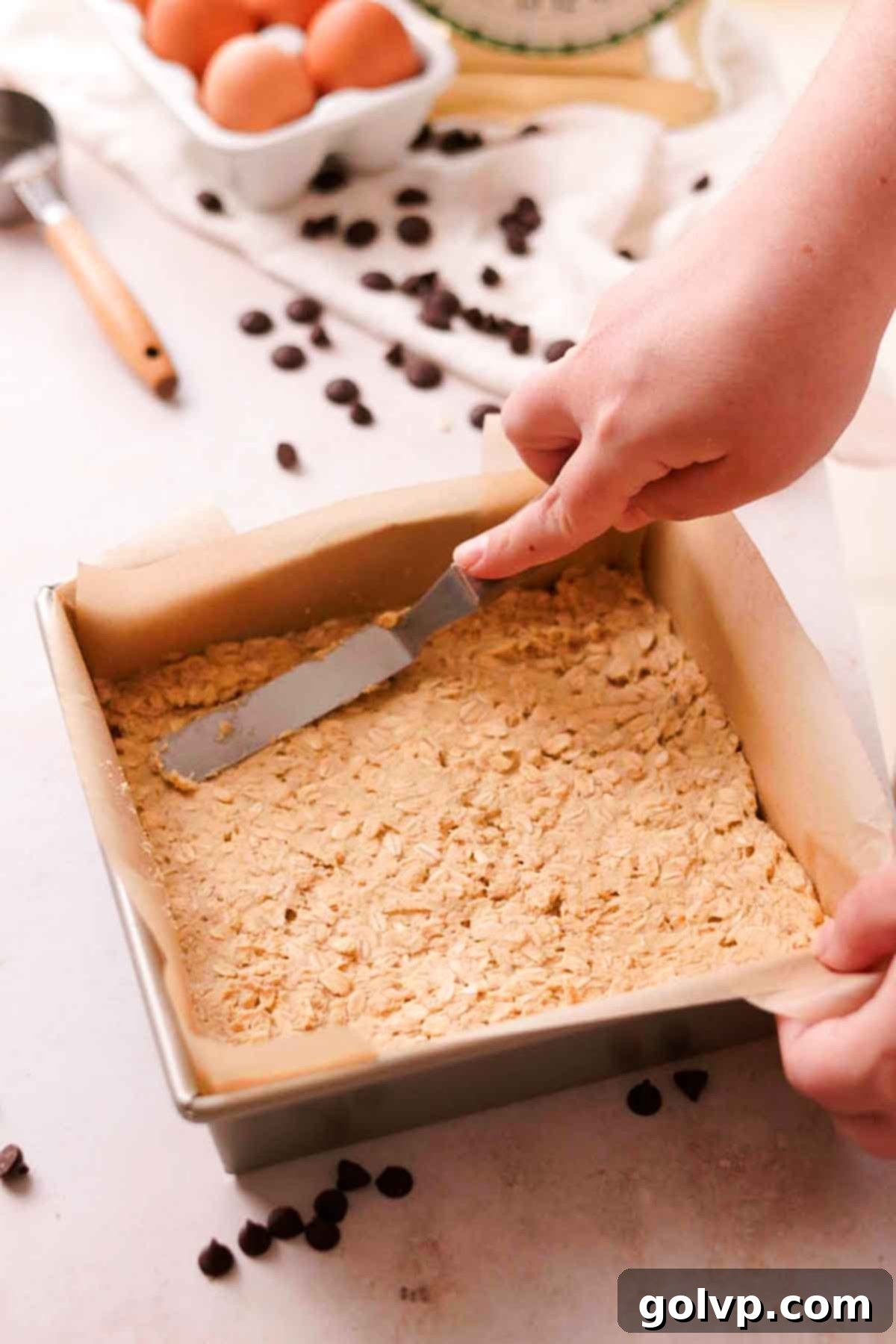 spreading oatmeal cookie dough in the bottom of a square baking pan