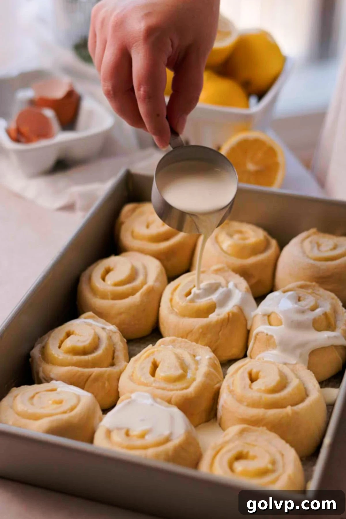 Pouring heavy cream over the lemon rolls in a baking pan before baking.