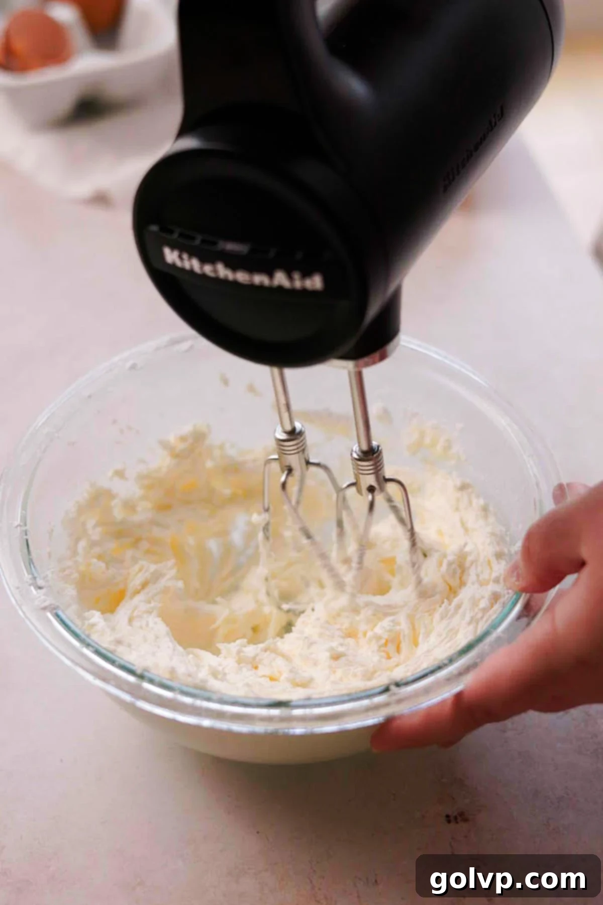 Beating softened butter and powdered sugar together in a bowl with an electric mixer for the frosting.