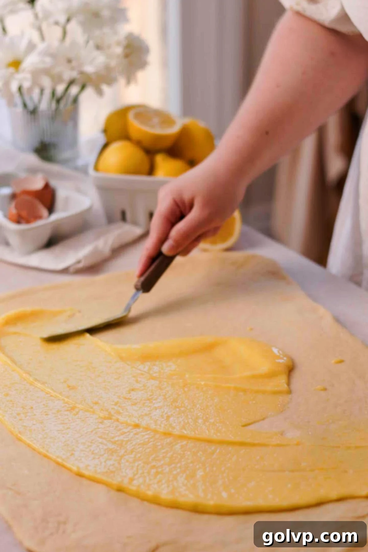 Spreading the lemon curd mixture evenly over the rolled-out dough.