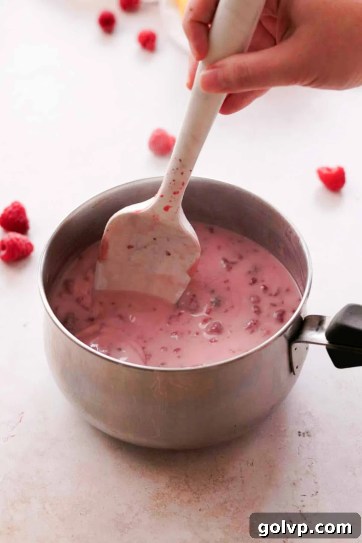 stirring raspberries and cream with silicone spatula in saucepan