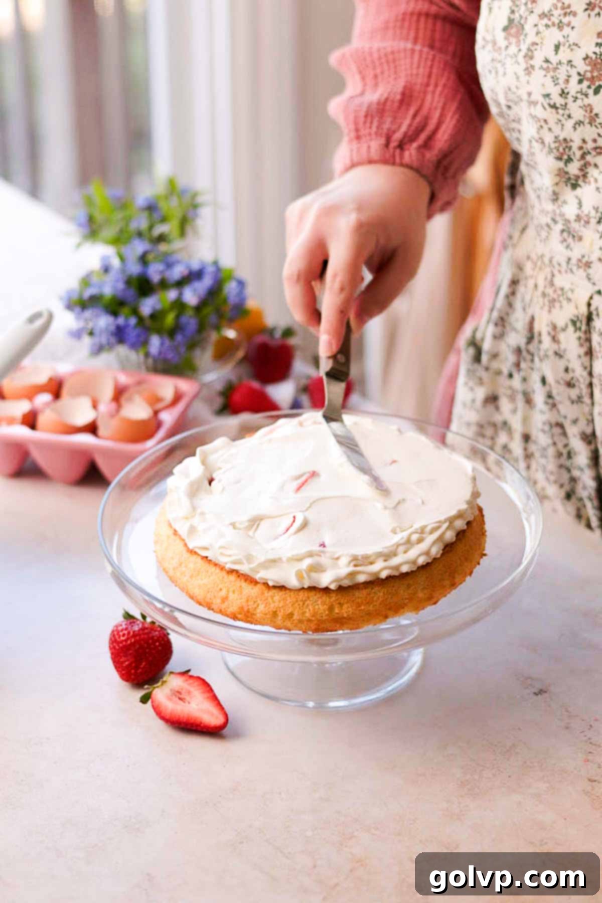covering macerated strawberries with whipped cream frosting and smoothing with spatula