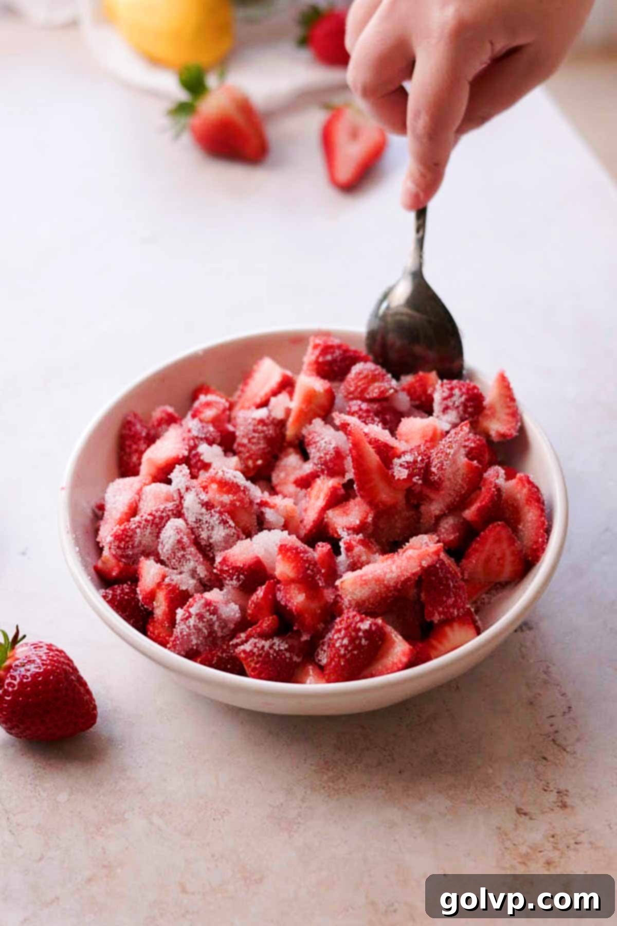 stirring strawberries coated in sugar in a bowl with a spoon