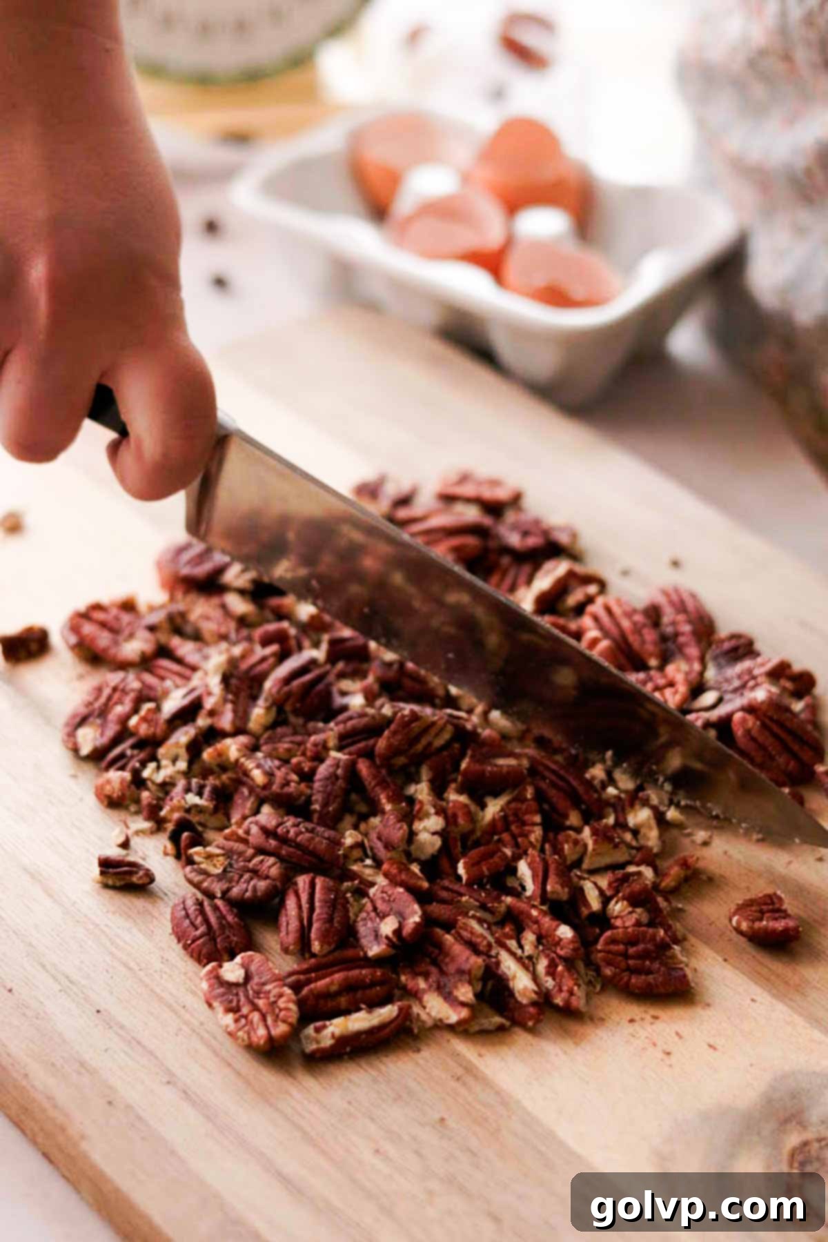 chopping pecans with a knife on a wooden cutting board