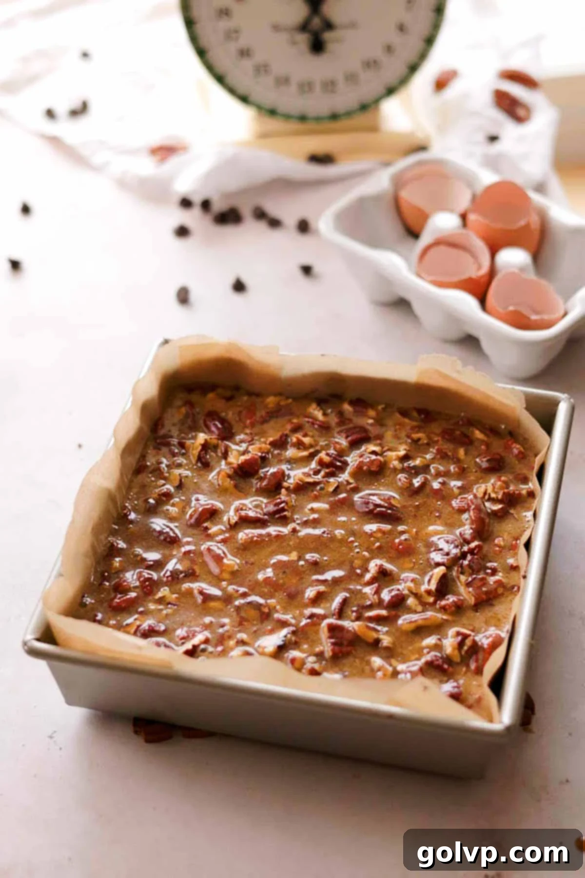 brownie batter in a square tin pan with an even layer of pecan butter topping spread on top