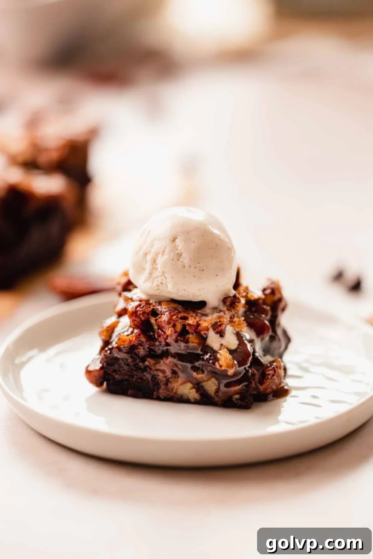 a pecan brownie square with a scoop of vanilla bean ice cream on top sitting on a plate