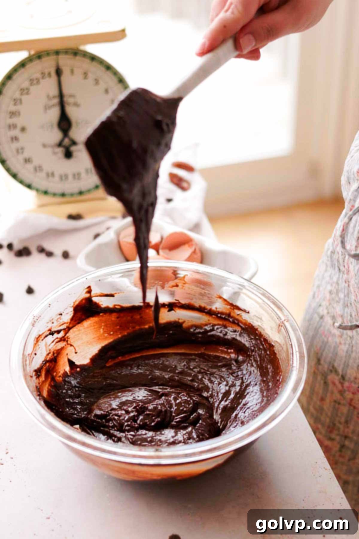 raw brownie batter falling off of a silicone spatula into a bowl of batter, showing the rich chocolate color
