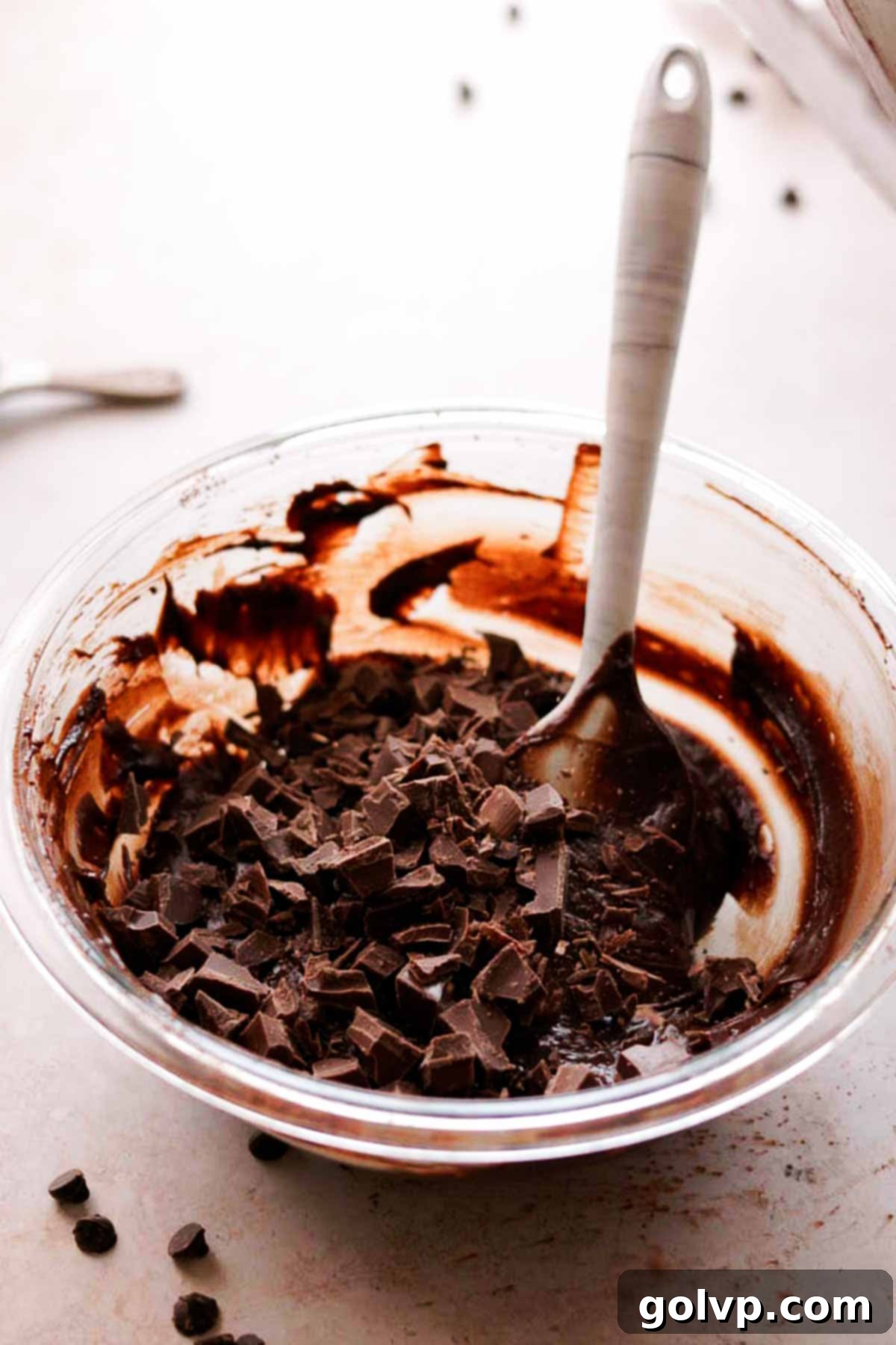 chocolate chips being added to the brownie batter in a glass bowl