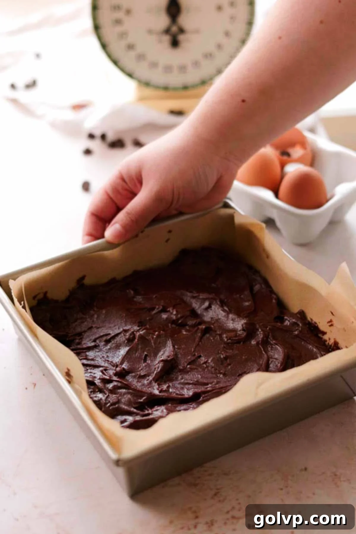 spread brownie batter in a square tin pan with parchment paper