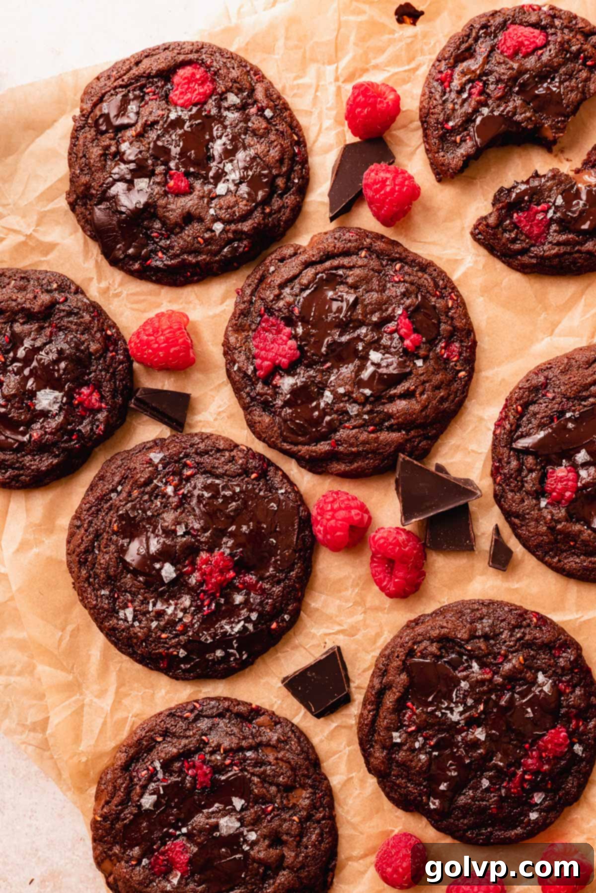 chocolate raspberry cookies on brown parchment paper with chocolate pieces and fresh raspberries around