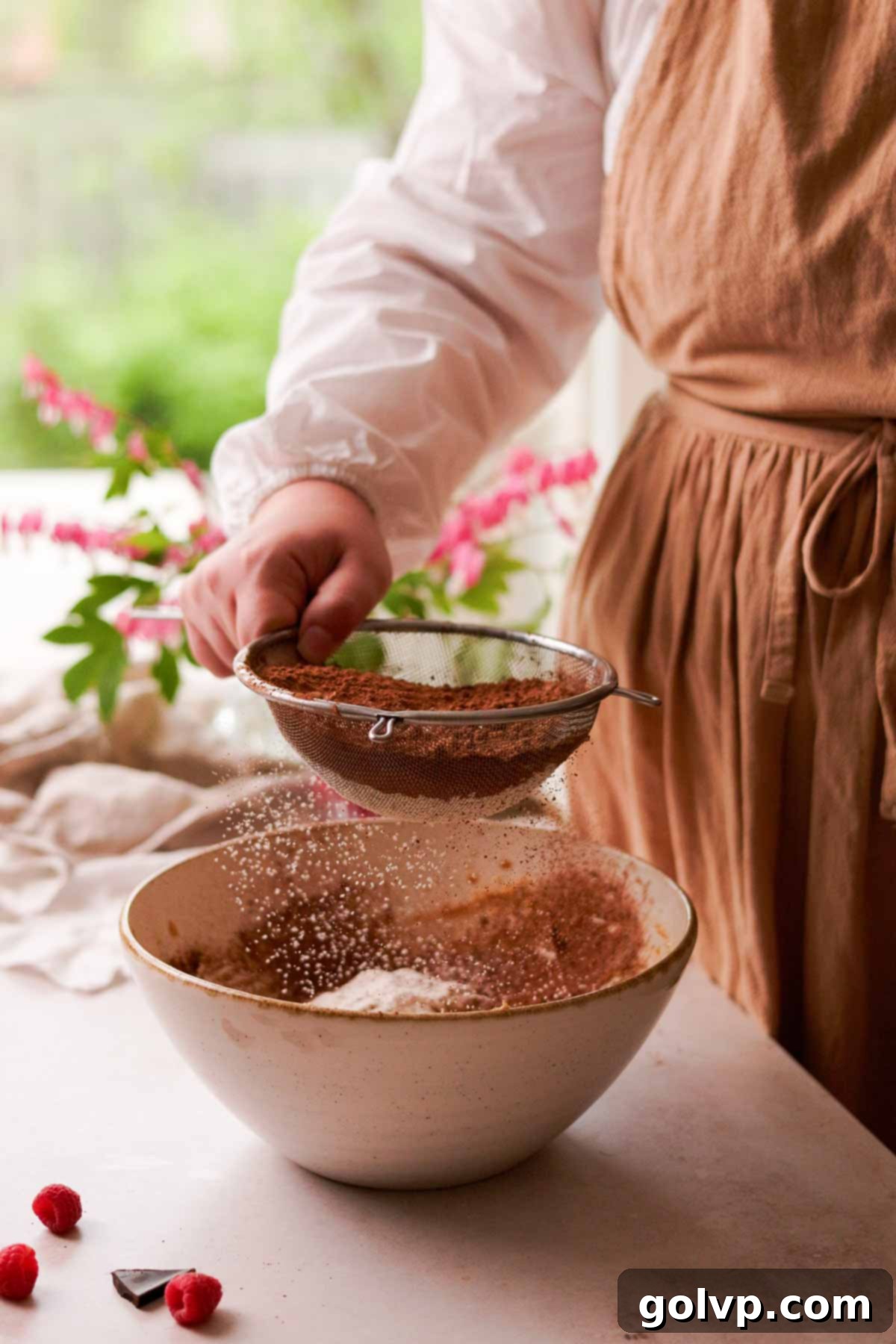 sifting cocoa powder and flour into a bowl of cookie dough mix