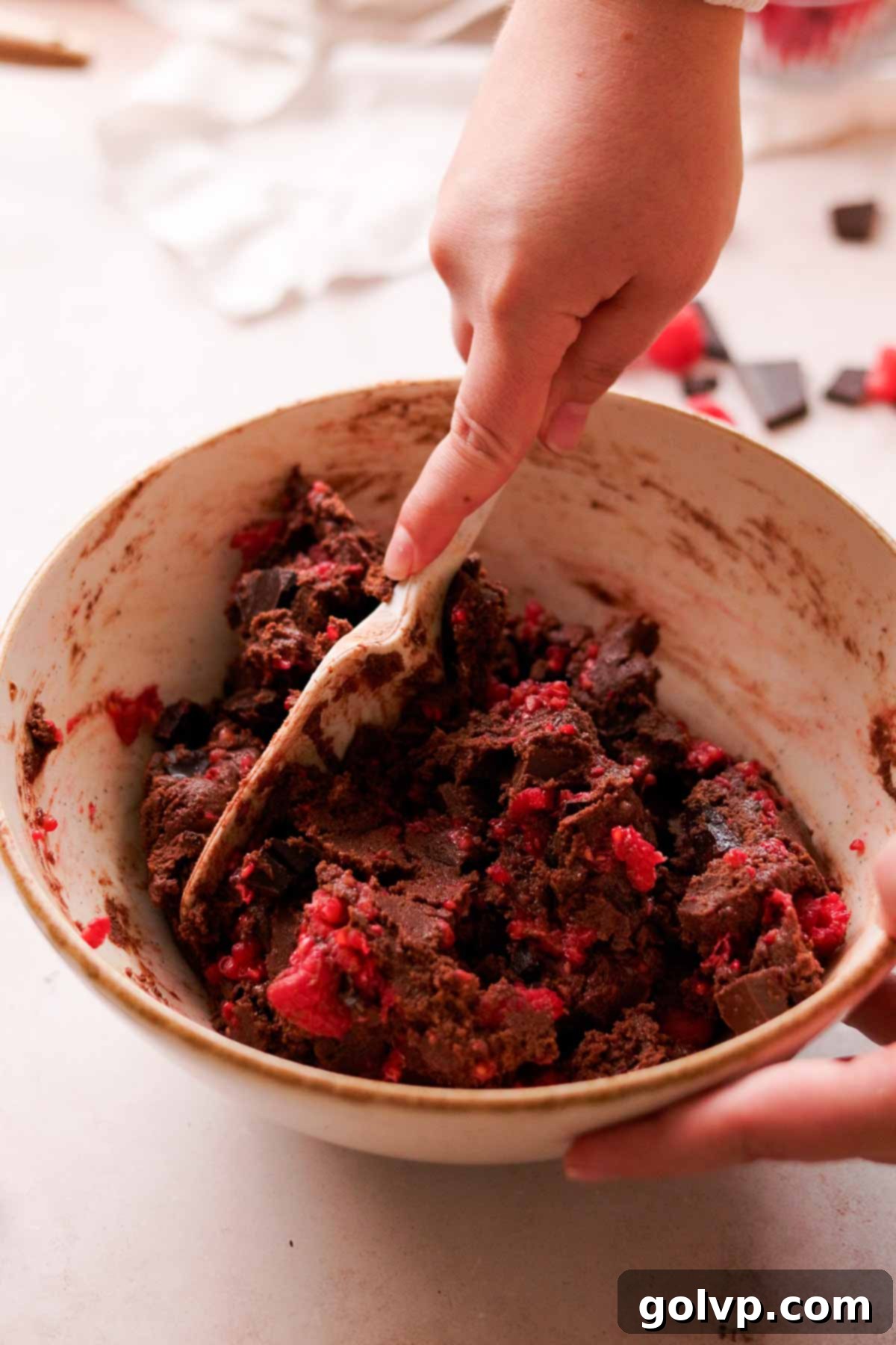 folding broken chocolate chunks and fresh raspberry into cookie dough