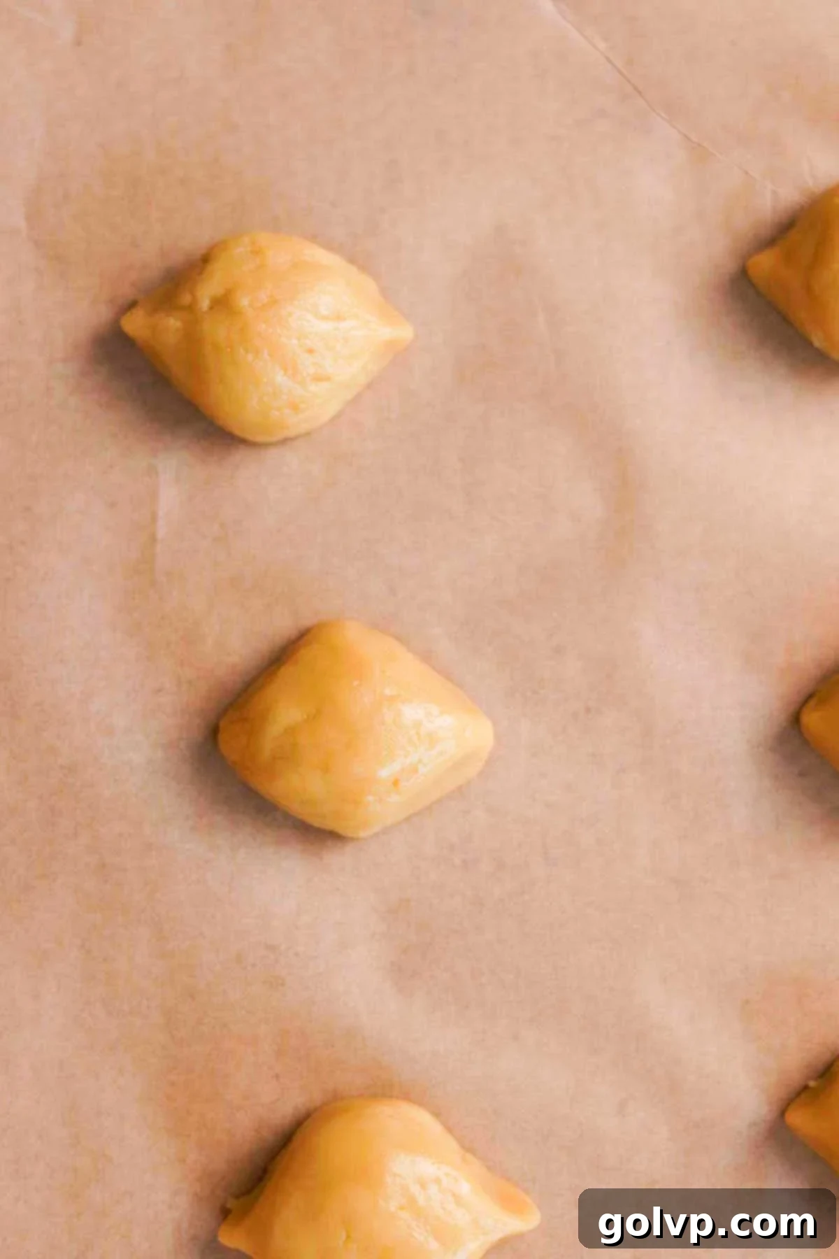Lemon-shaped cookie dough balls neatly arranged on brown parchment paper, ready for baking.