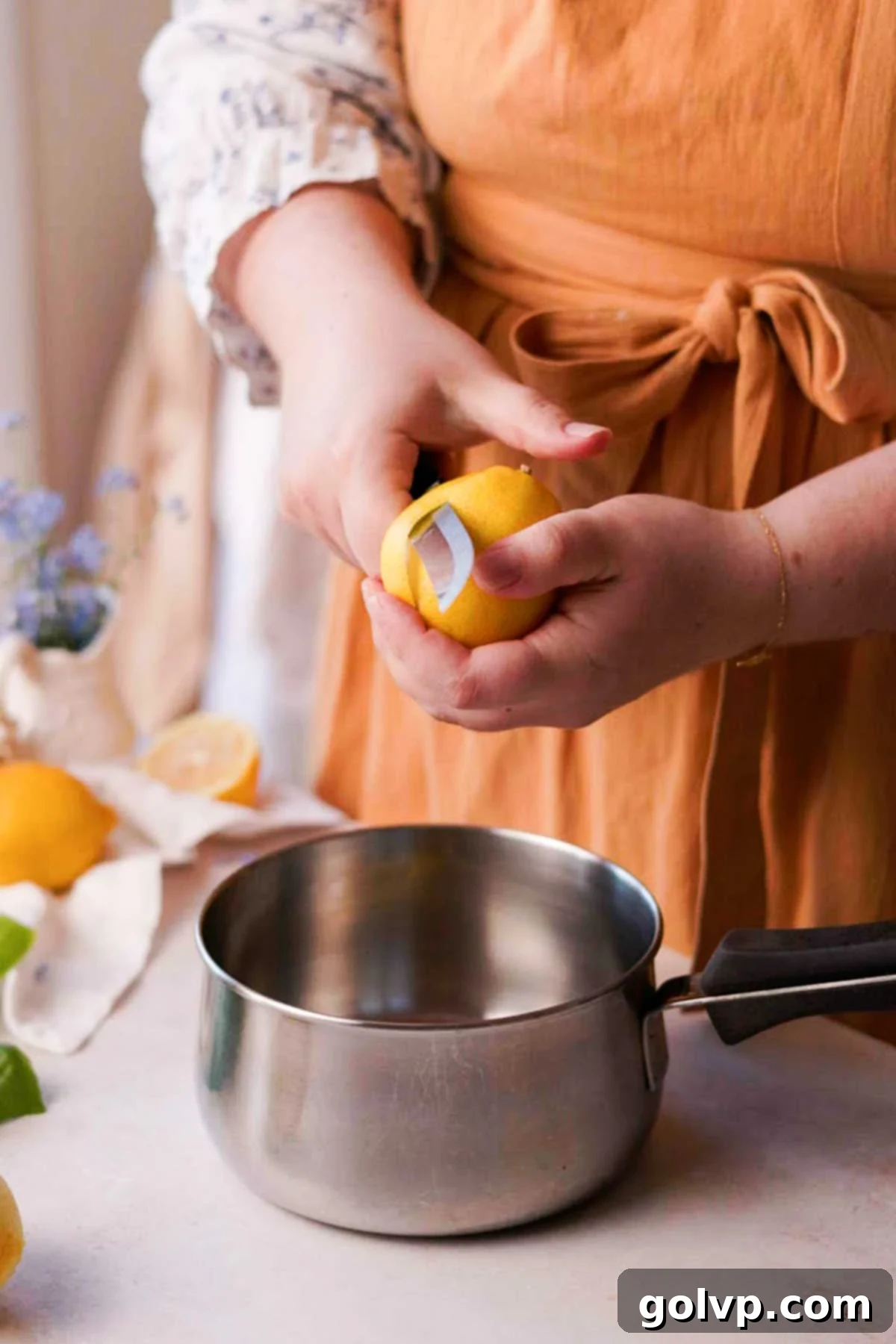 Using a knife to carefully peel bright yellow lemon zest into a saucepan for the syrup, ensuring no white pith is included.