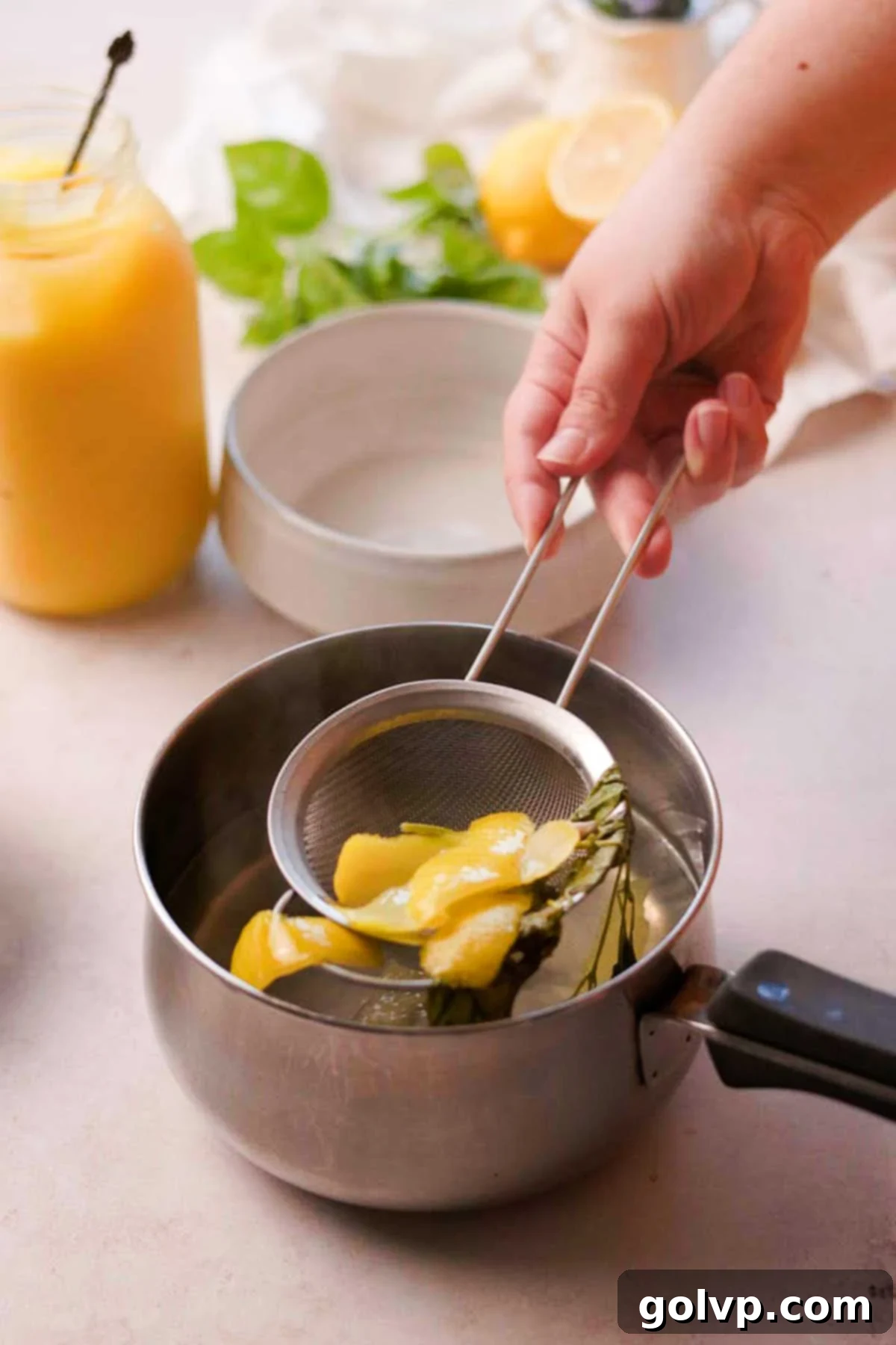 Straining the fragrant basil sprigs and lemon zest out of the finished lemon basil syrup, leaving a clear, infused liquid.
