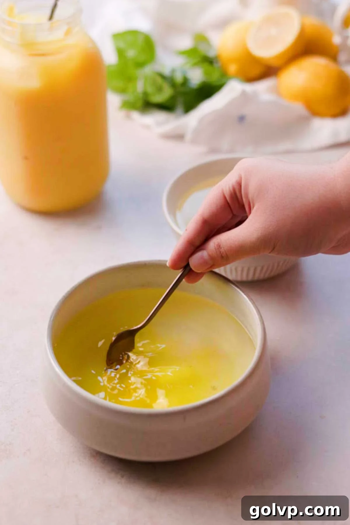 A teaspoon of bright yellow food coloring being added to a small bowl of lemon syrup, preparing it for coloring the cookies.