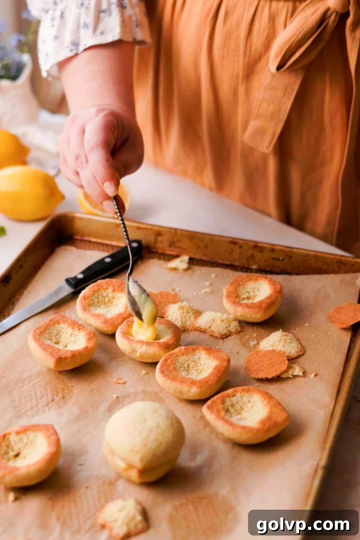 Piping or spooning tangy lemon curd into the hollowed-out centers of baked Italian lemon cookies, ready for assembly.