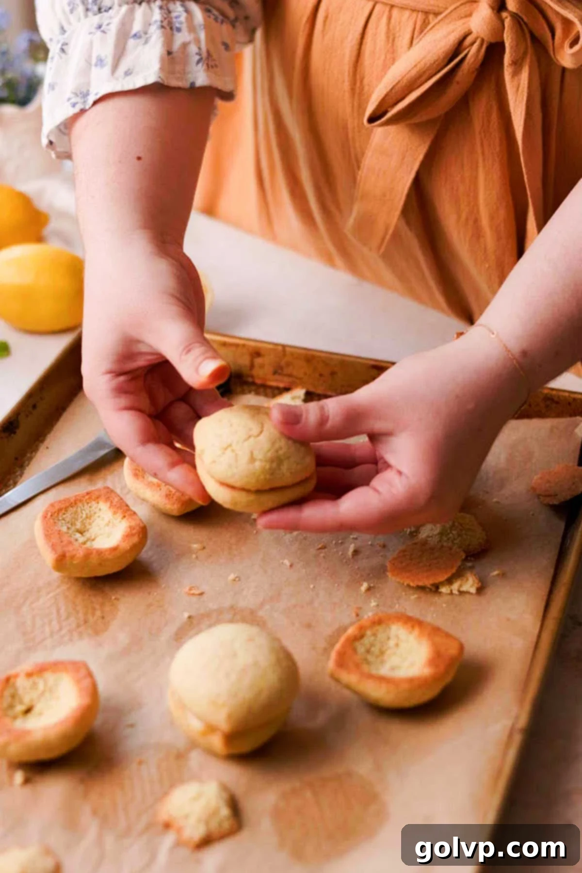 Gently pressing two lemon curd-filled cookie halves together to form a complete Italian lemon cookie shape.