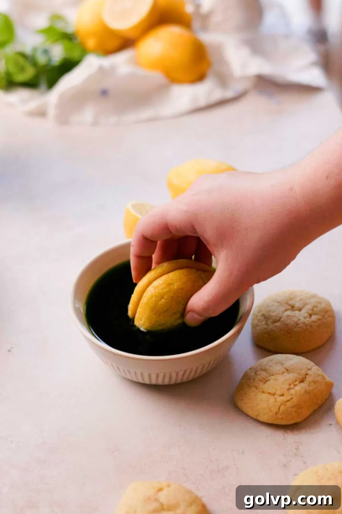 An Italian lemon cookie being briefly dipped halfway into vibrant green syrup, creating a two-toned effect.