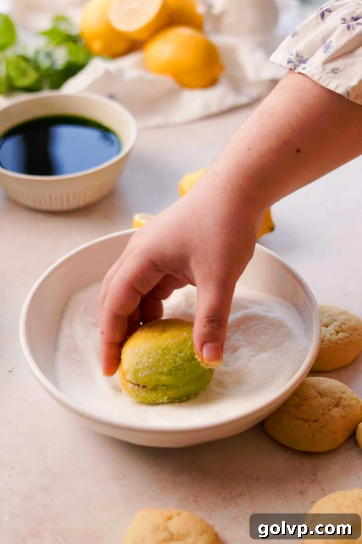 A freshly dipped Italian lemon cookie being rolled in a bowl of granulated sugar for a sweet, sparkling finish.