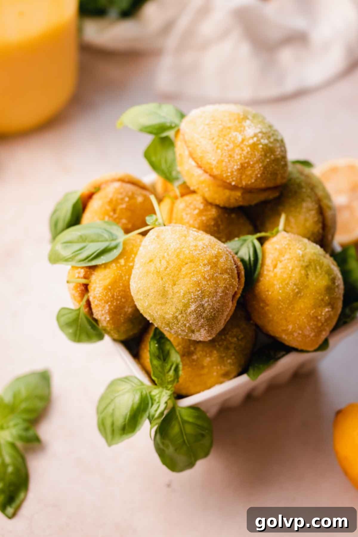 A beautiful arrangement of Italian wedding lemon cookies, sugar-coated and garnished with fresh basil leaves, presented in a rustic bowl.