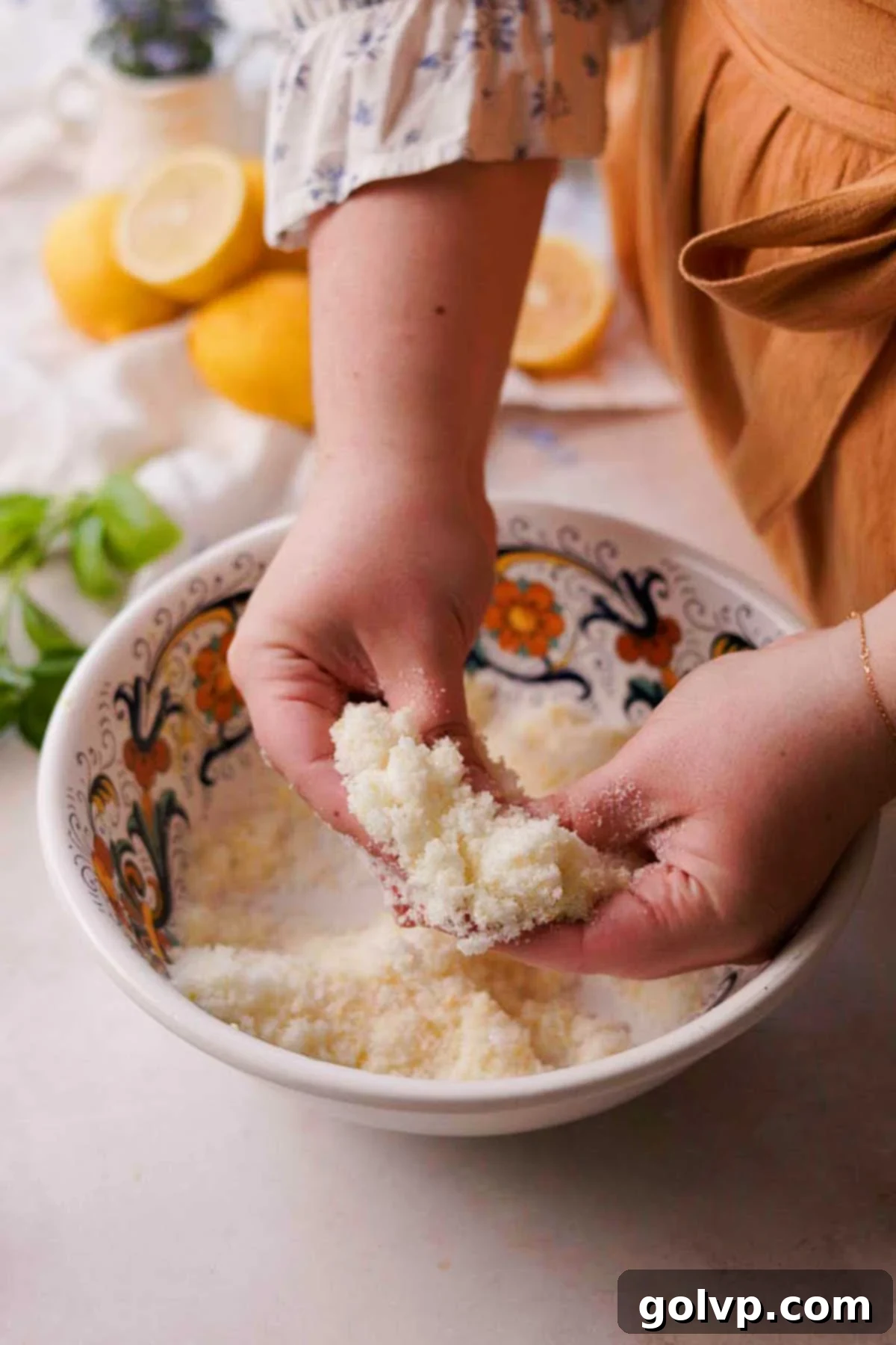 Hands rubbing granulated sugar and vibrant lemon zest together in a mixing bowl, releasing the fragrant citrus oils into the sugar.