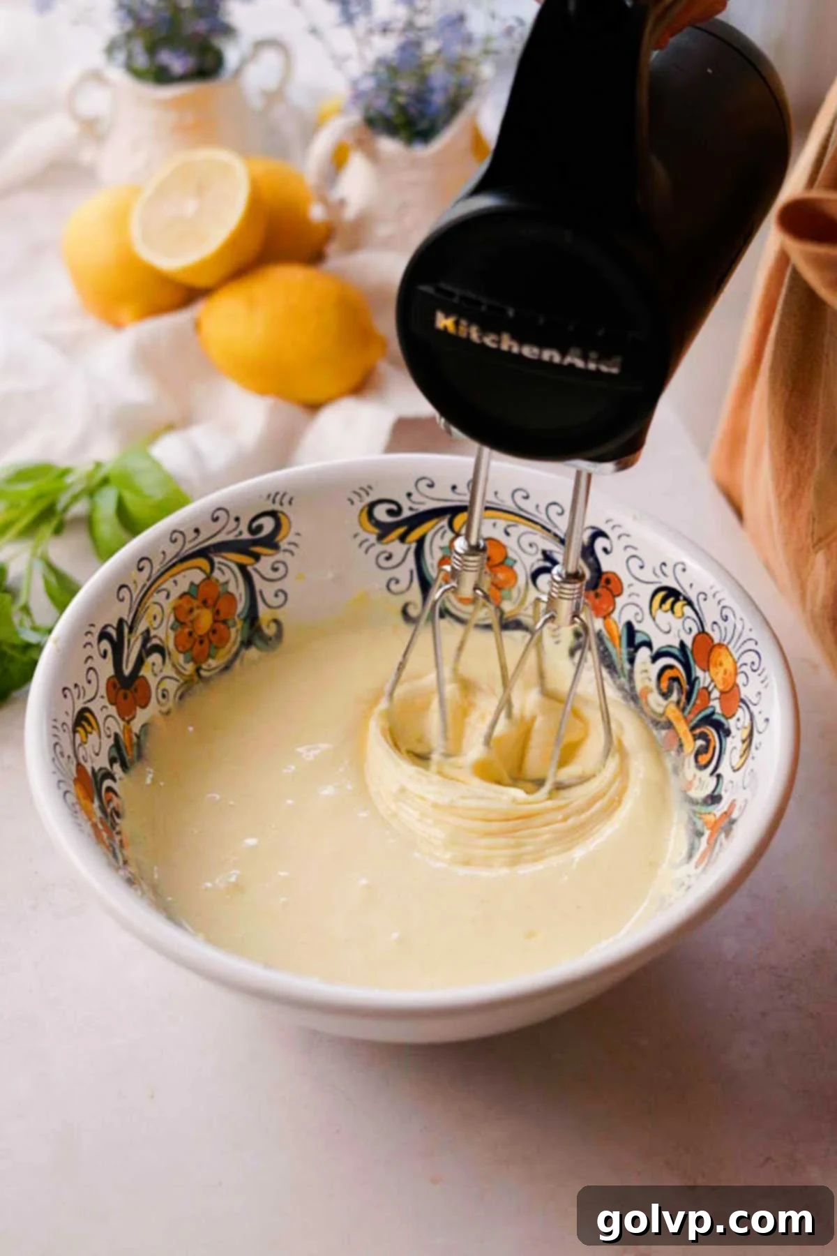 An electric whisk expertly beating eggs and lemon-infused sugar in a mixing bowl, creating a thick, creamy, and lightened mixture.