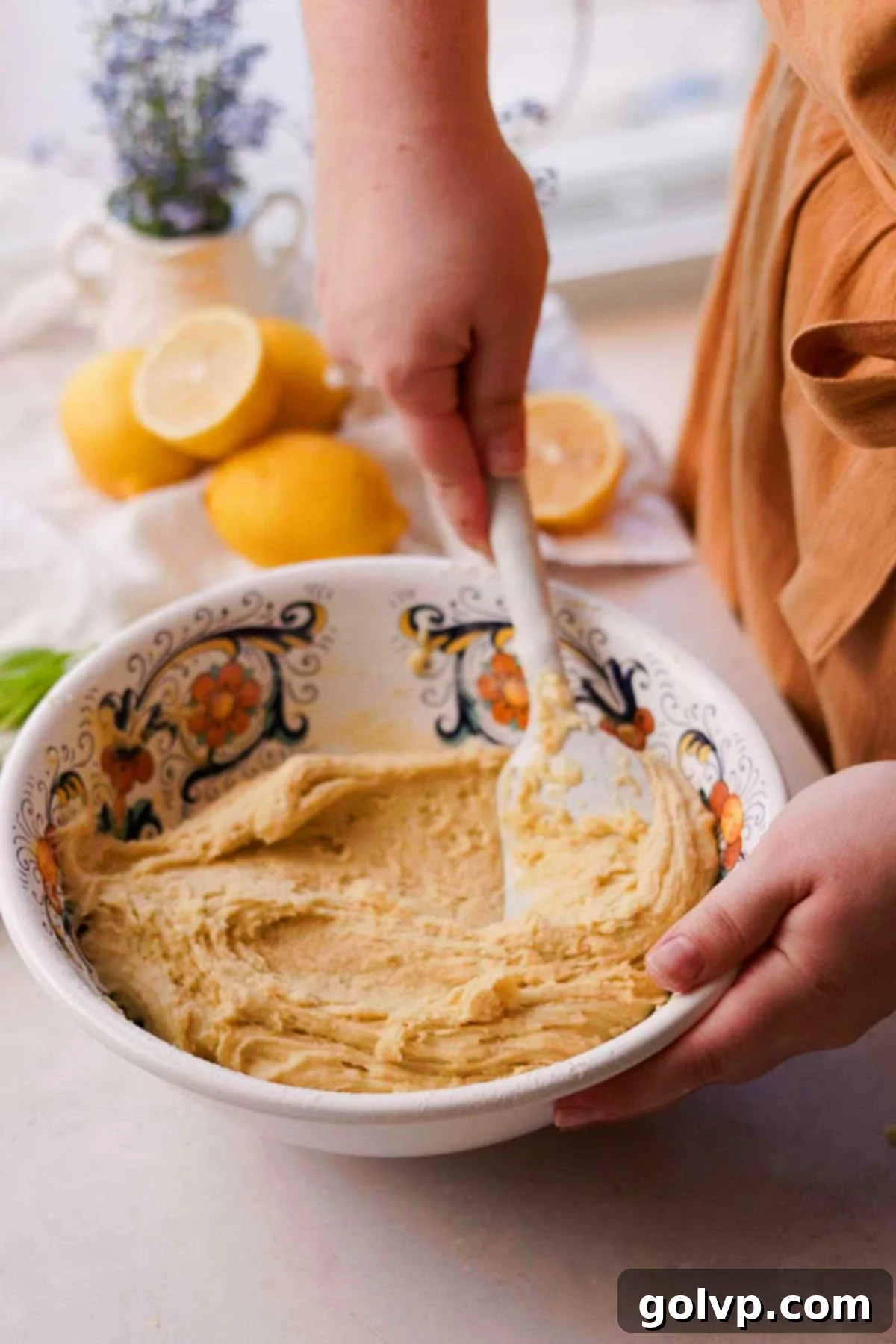 A spatula gently folding flour and baking powder into the lemon olive oil cookie dough, creating a smooth and soft consistency.