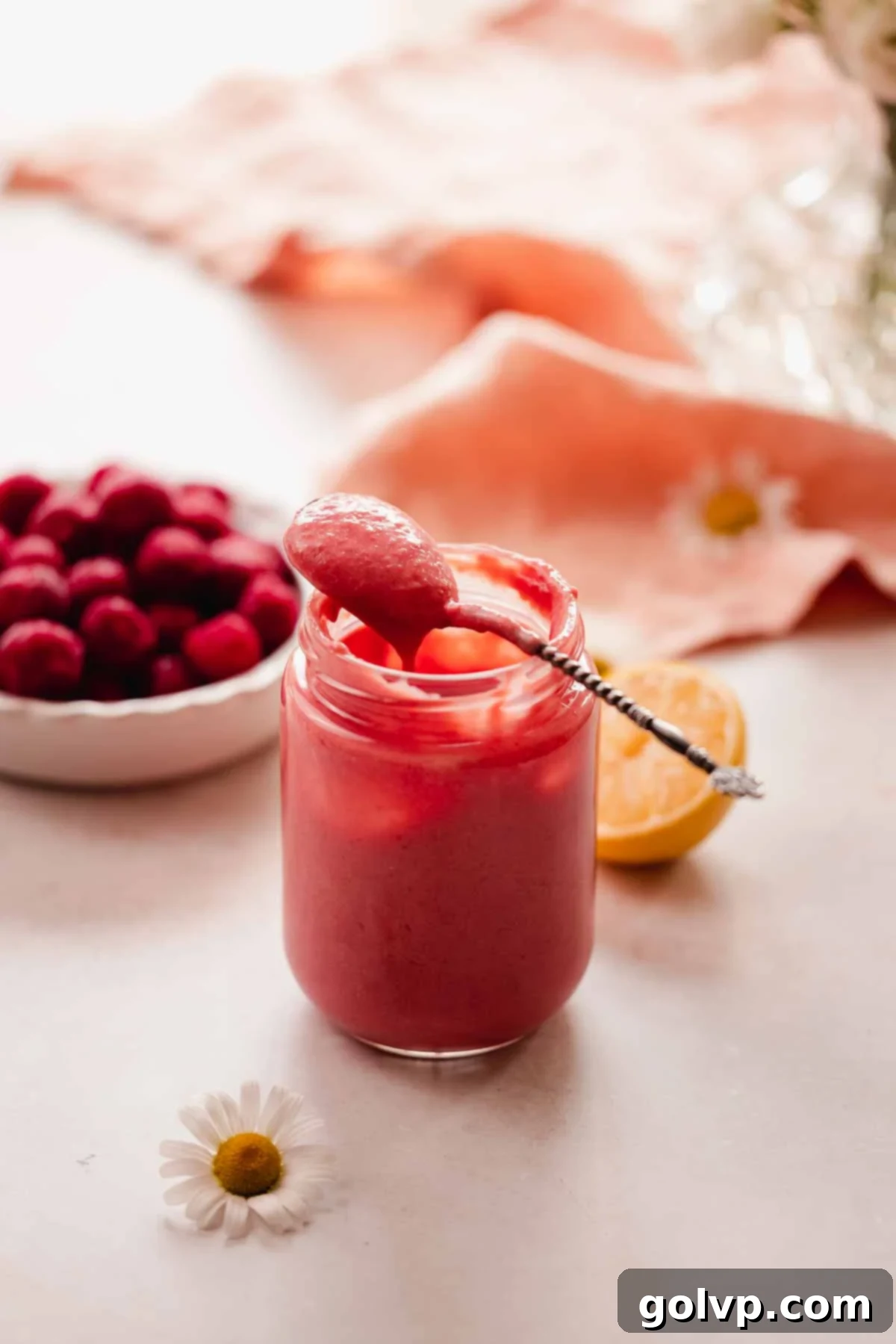 cherry curd dripping off spoon resting on the edge of a jar