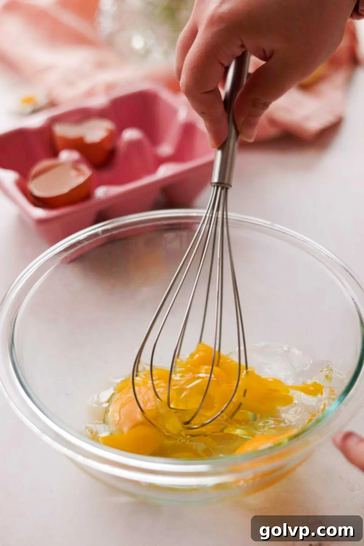 whisking eggs in a glass bowl with a metal whisk by hand