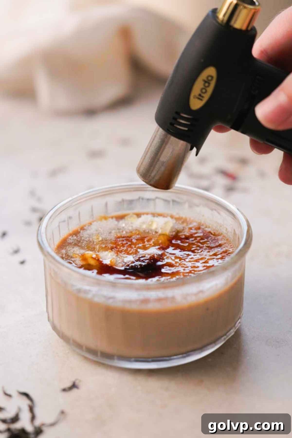 Granulated sugar being sprinkled on chilled crème brûlée for torched topping