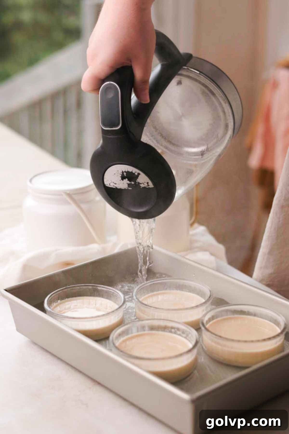 Boiling water being poured into a baking tray around ramekins