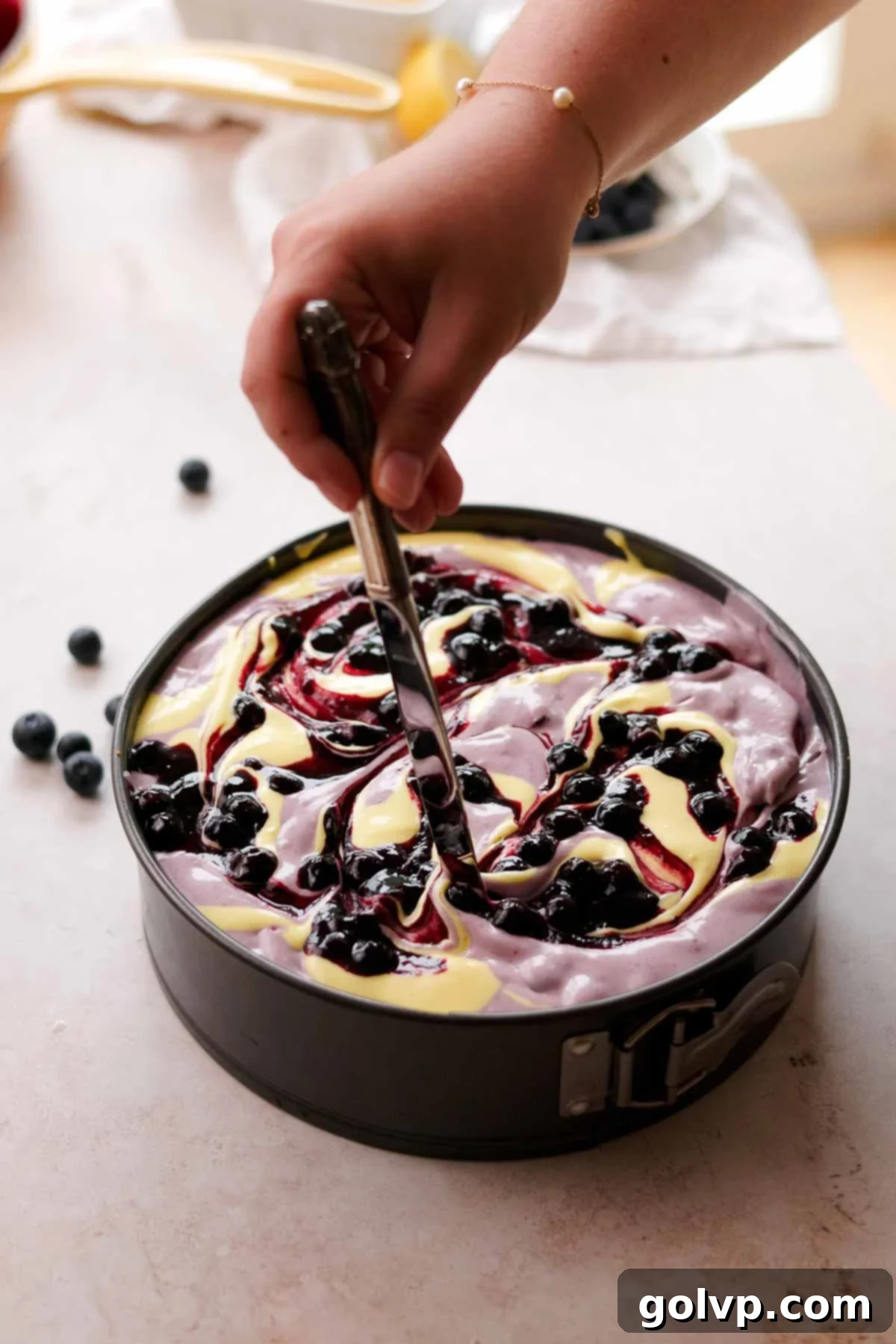 swirling blueberry lemon cheesecake batter with blueberries on top