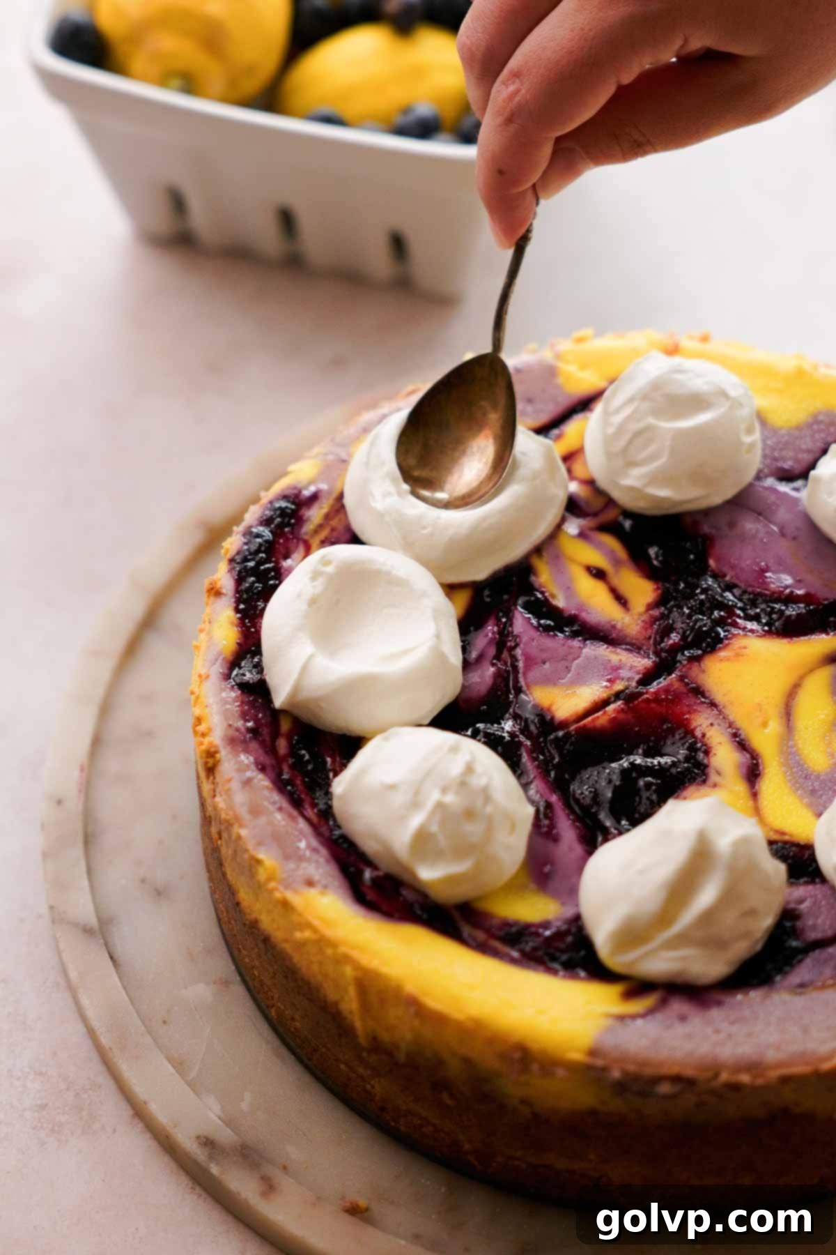 making dollops of whipped cream with a spoon on top of the blueberry lemon cheesecake