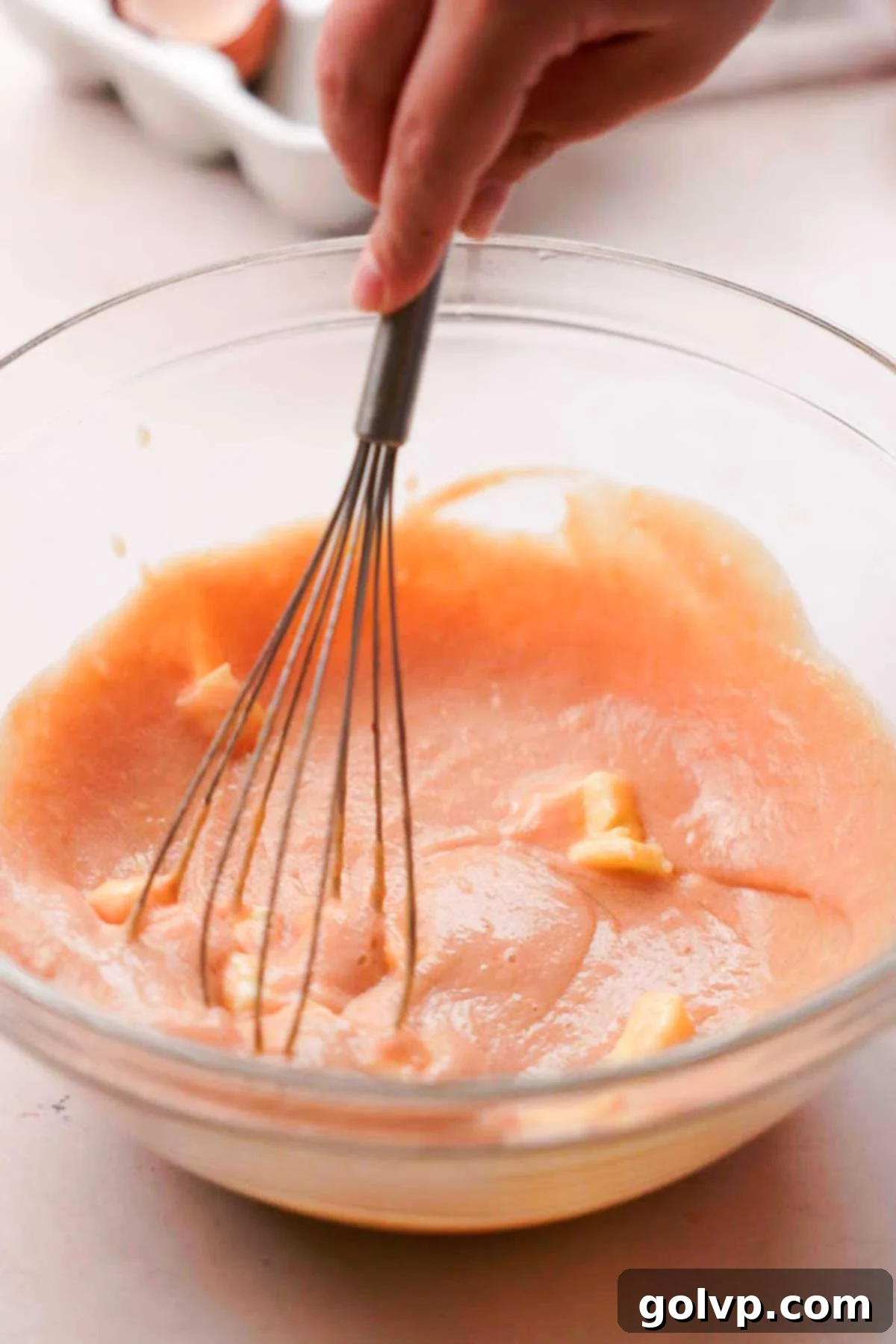 Adding cubes of butter and a pinch of salt to the strained peach curd and whisking until smooth