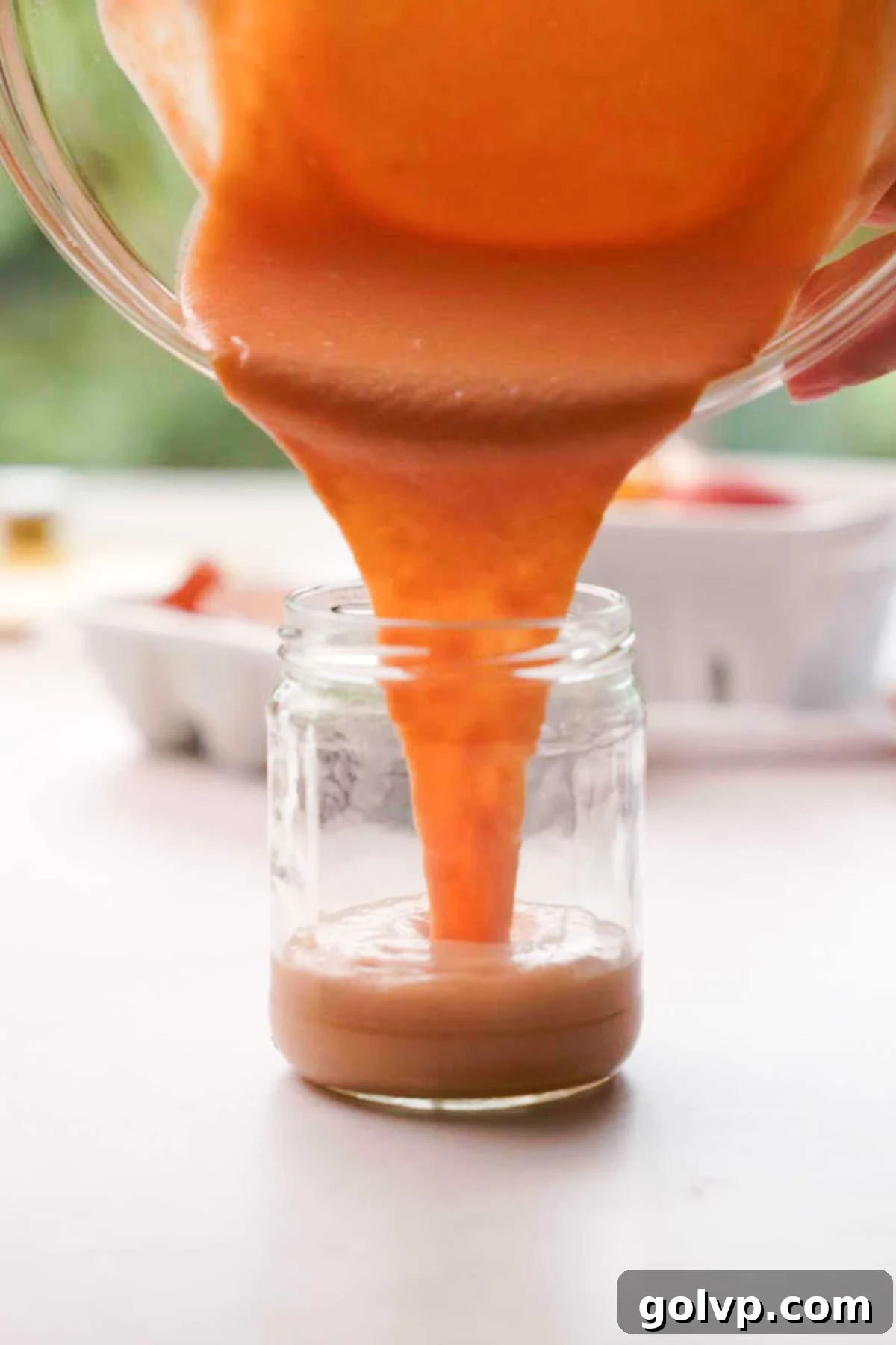 Pouring the freshly made peach curd from a bowl into a smaller glass jar for chilling