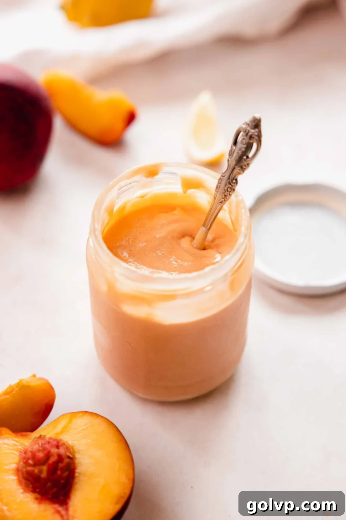 Glass jar filled with peach curd, a spoon dipped inside, ready to be enjoyed