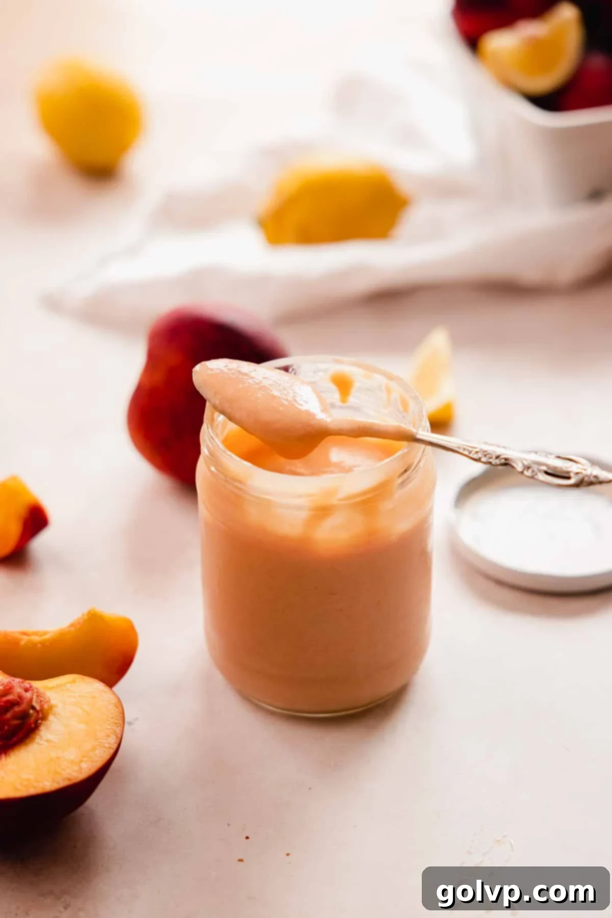 A spoonful of smooth peach curd resting on the rim of a glass jar