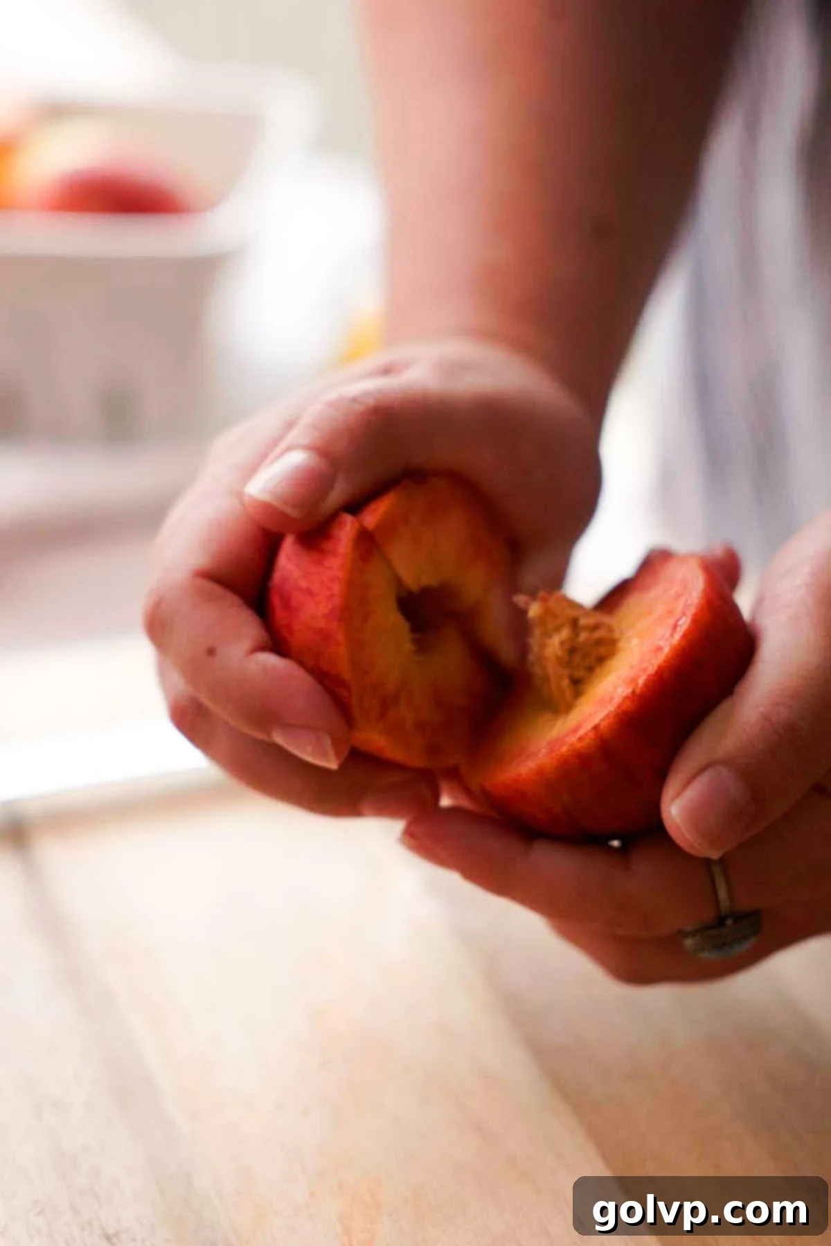 Twisting a cut peach by hand to separate its halves from the stone
