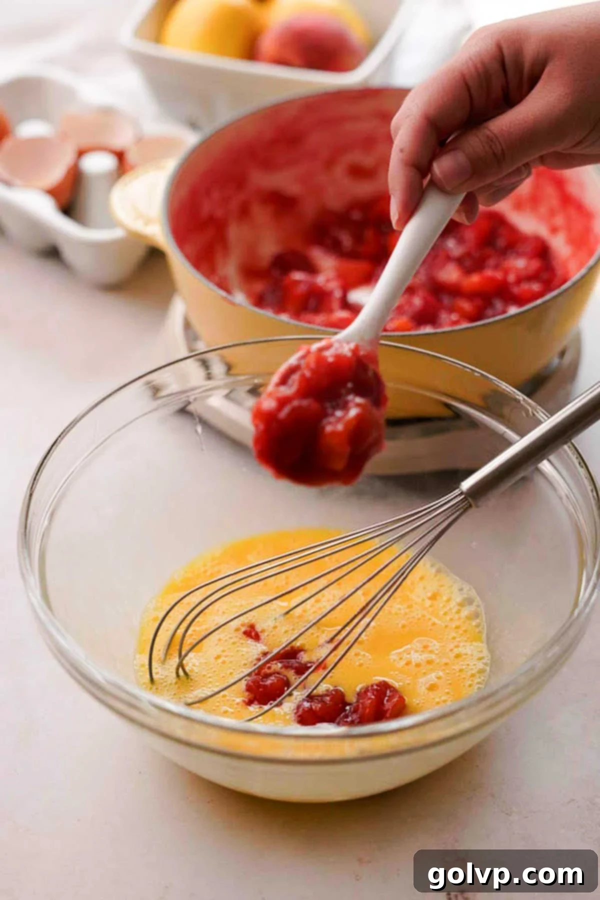 Carefully adding hot peach mixture spoonful by spoonful into whisked eggs, while continuously whisking
