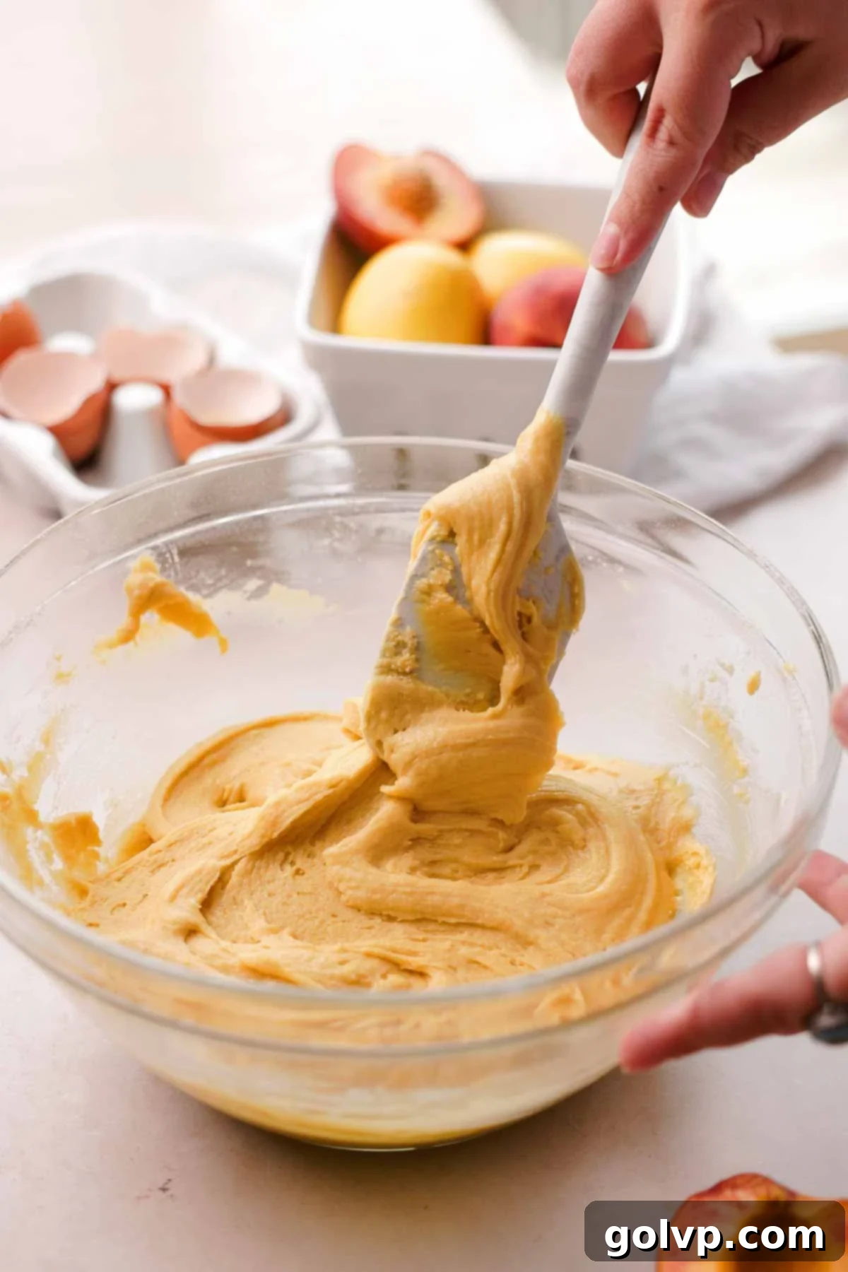folding peach cookie dough in a glass bowl with a spatula