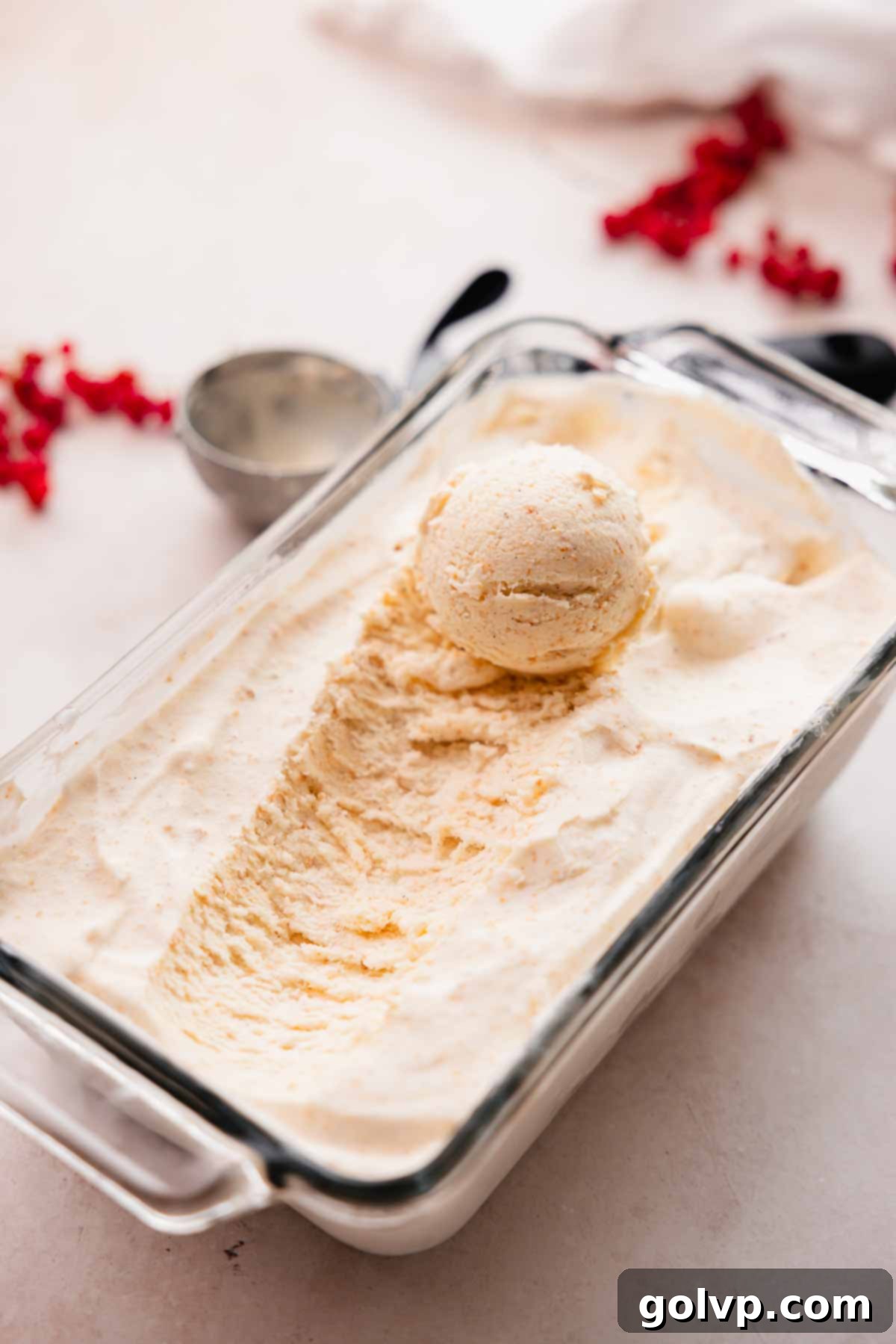 Glass tray full of creamy brown butter ice cream with a metal scoop resting on top, ready to serve.